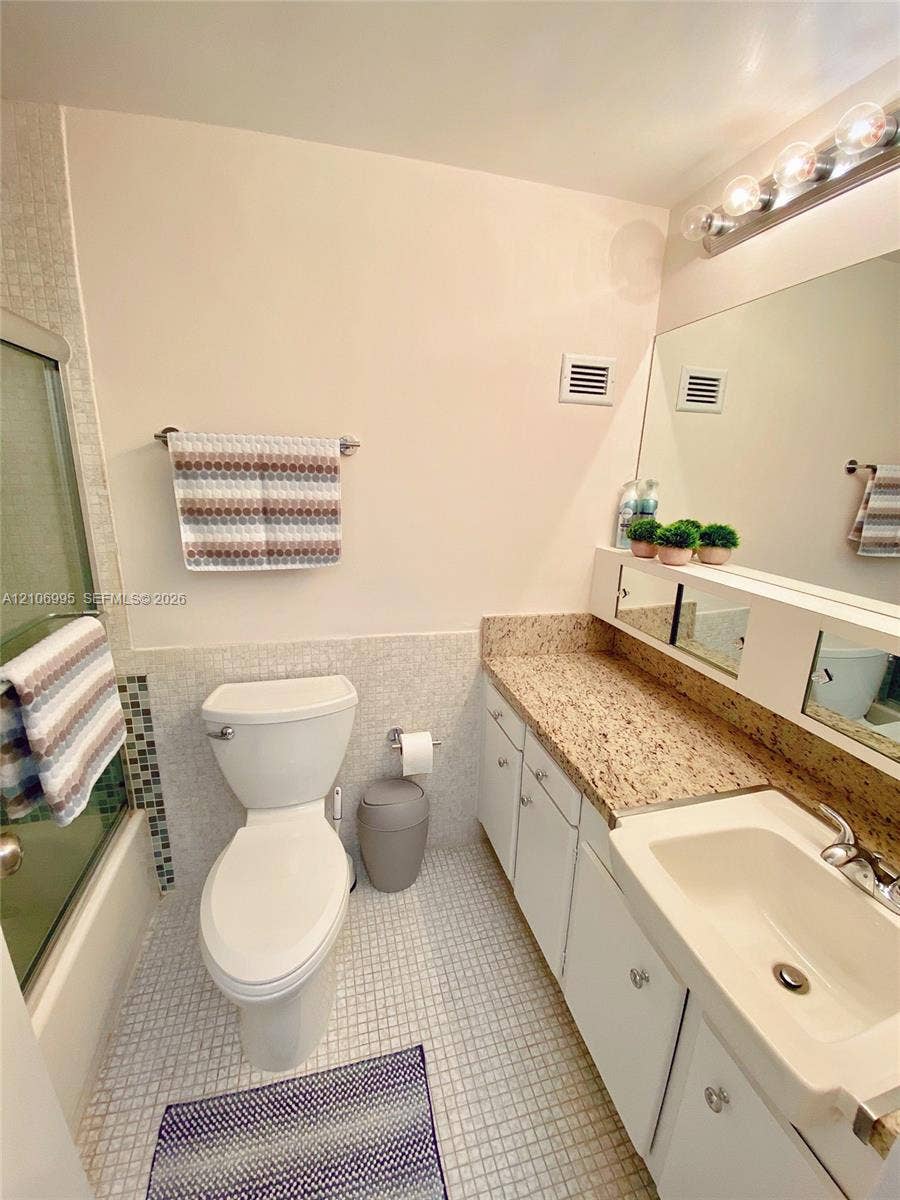 3505 S Ocean Drive, #1404, Hollywood, FL 33019 Bathroom featuring a vanity with stone-finish countertop, integrated sink, large wall-mounted mirror, mosaic tile surround, and glass-enclosed shower