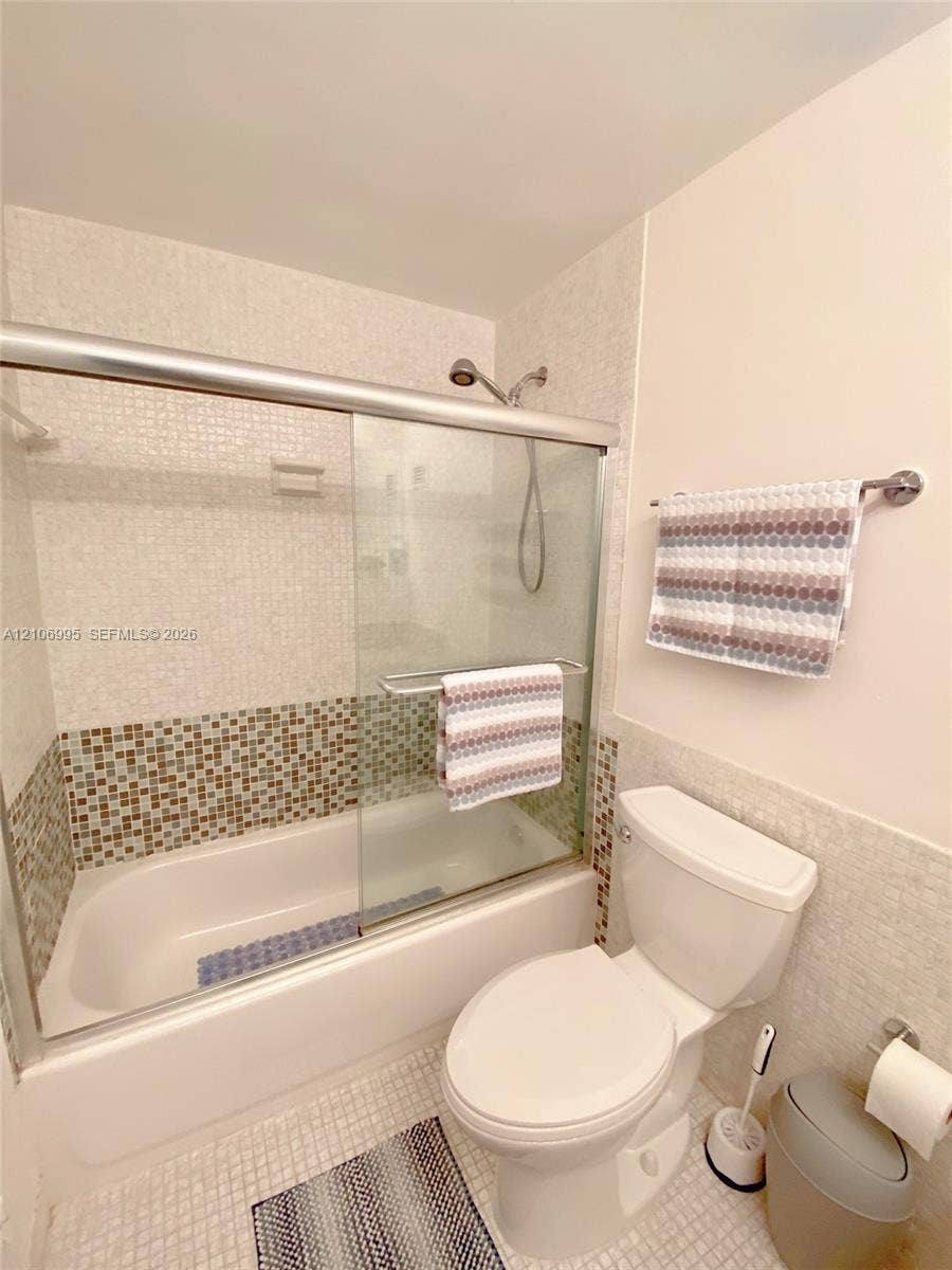 3505 S Ocean Drive, #1404, Hollywood, FL 33019 Bathroom featuring a shower-tub combination with sliding glass doors, multi-toned mosaic tile accents, and a wall-mounted hand-held shower head