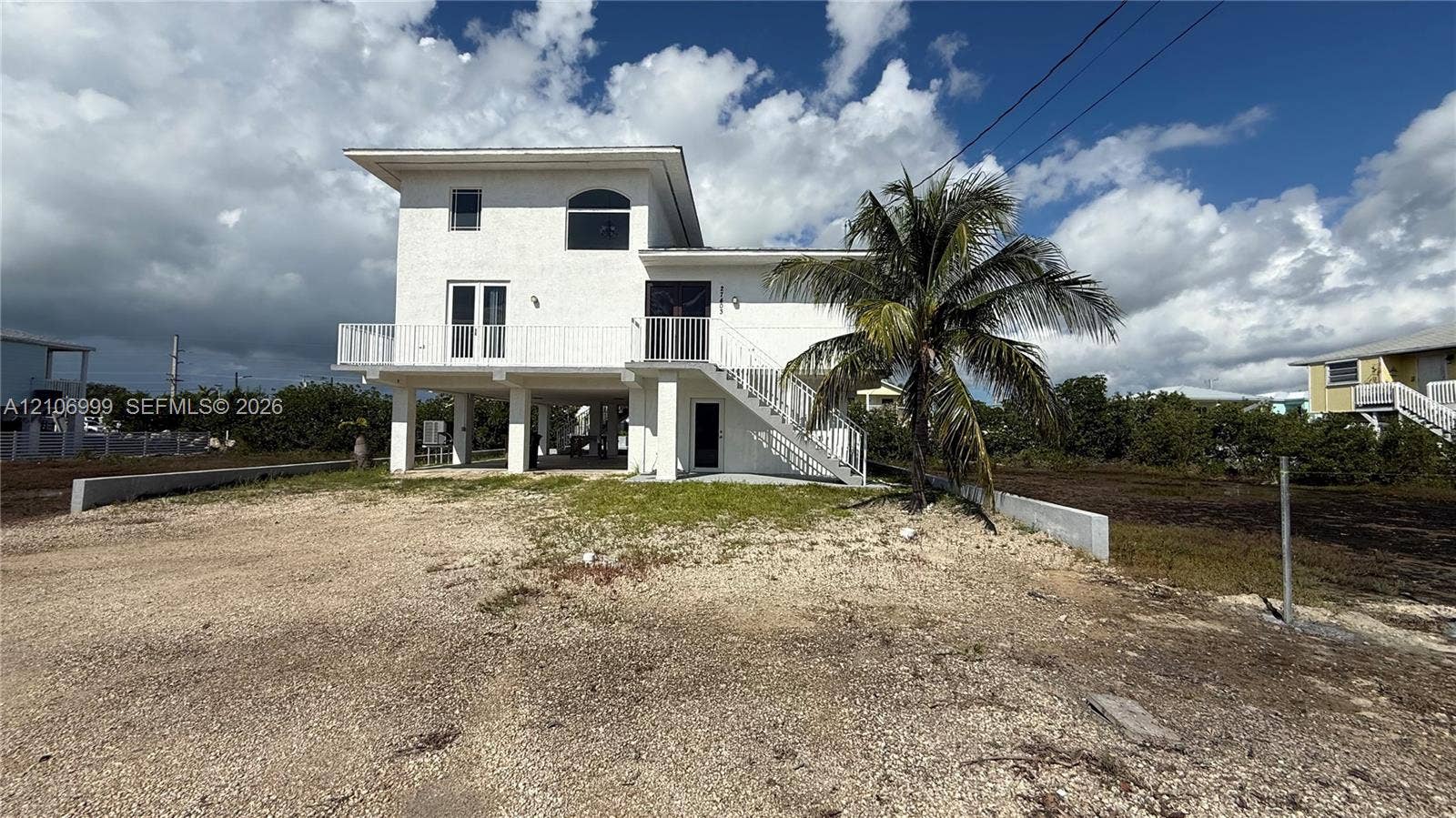 Stilted multi-level exterior with a white stucco facade, expansive elevated balcony, external staircase, and arched window detailing