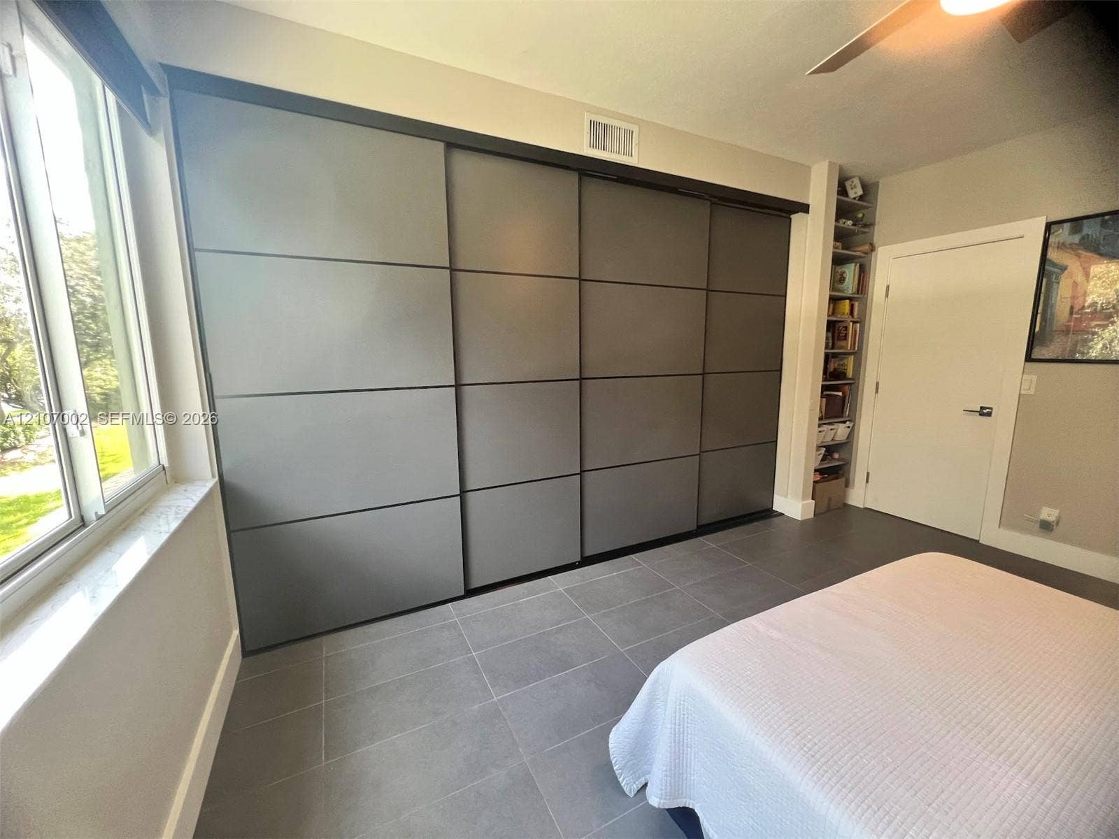 Large sliding closet system with a matte finish, expansive window with stone-finish sill, built-in floor-to-ceiling shelving, and tile flooring
