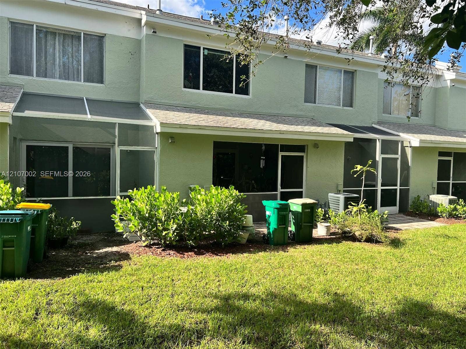 Stucco exterior featuring dual-level windows, a screen-enclosed patio, and asphalt shingle roofing
