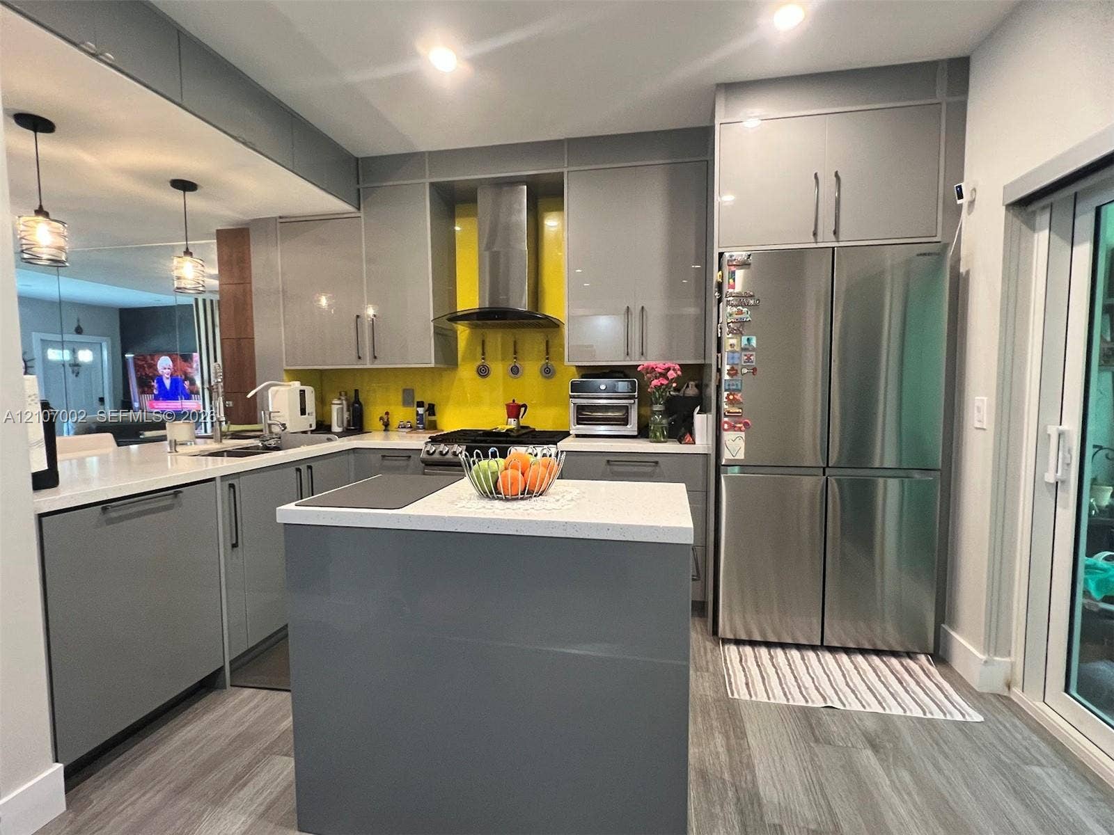 Kitchen featuring grey flat-panel cabinetry, a central island with a solid-surface countertop, stainless steel refrigerator, vibrant backsplash, and recessed lighting