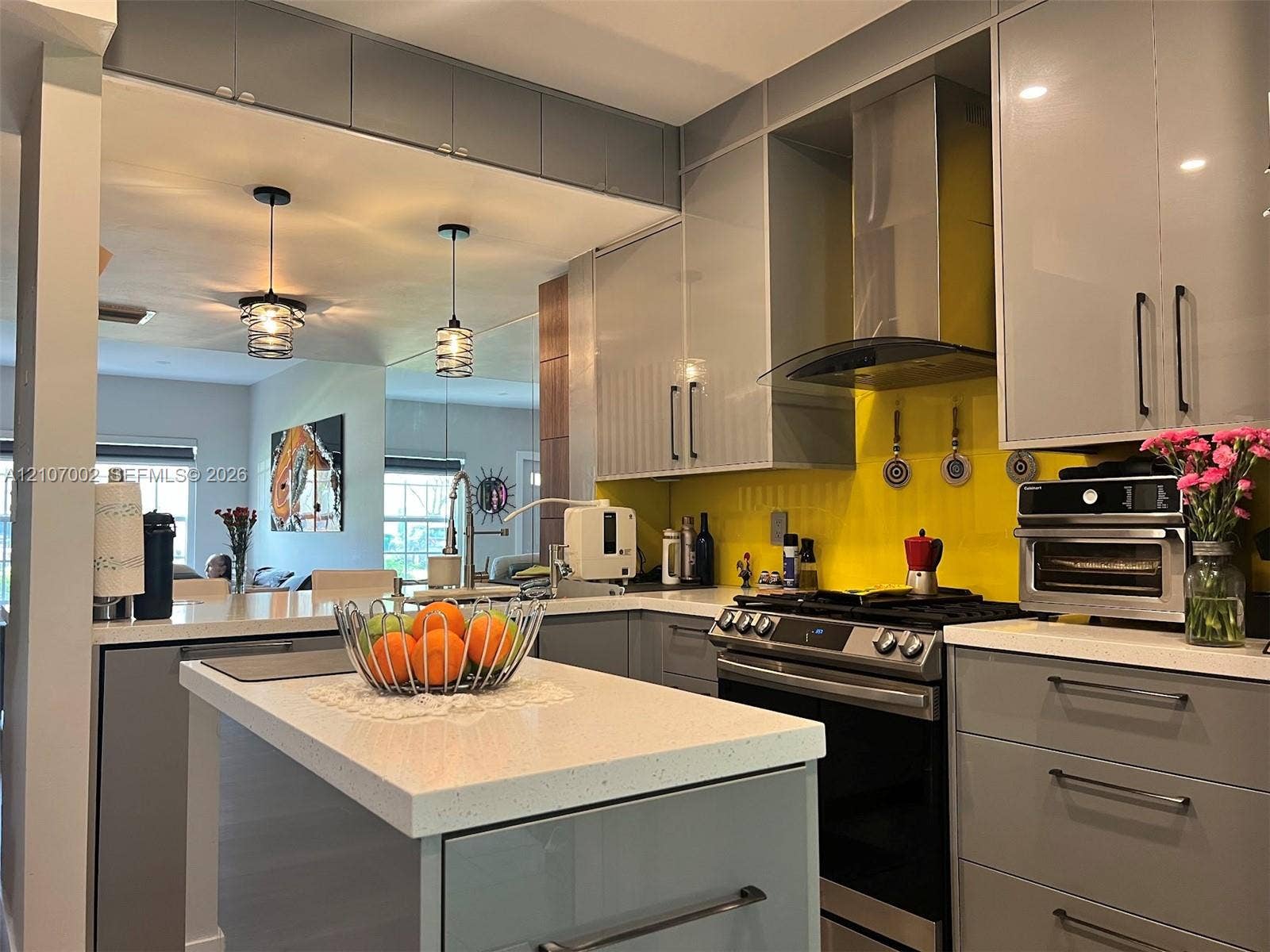 Contemporary kitchen featuring flat-panel cabinetry, a solid-surface island countertop, stainless steel range with overhead vent hood, and dual glass pendant lighting