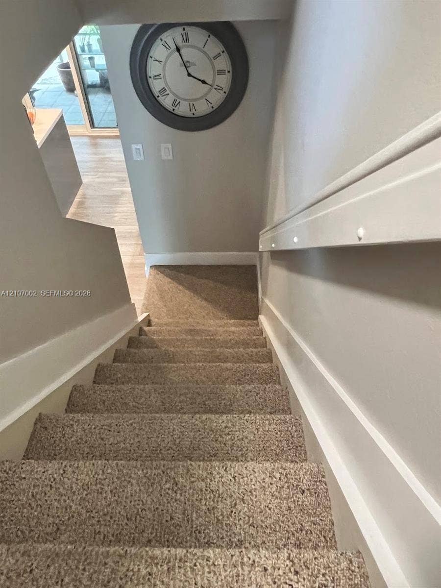 Staircase featuring wall-mounted lighting, neutral carpeting, and millwork detail