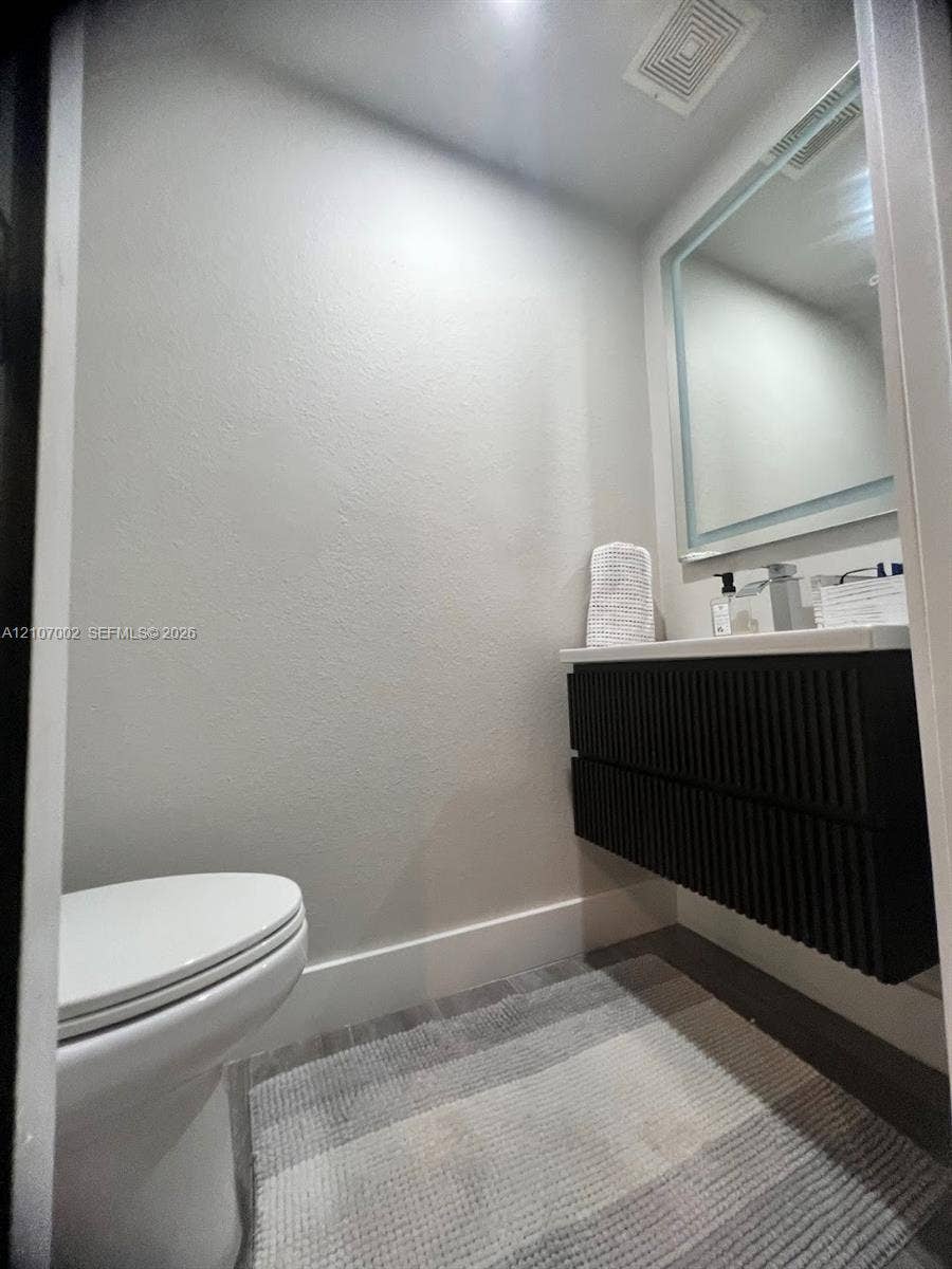 Wall-mounted vanity featuring a ribbed black finish, white countertop, integrated basin, and a rectangular LED-backlit mirror