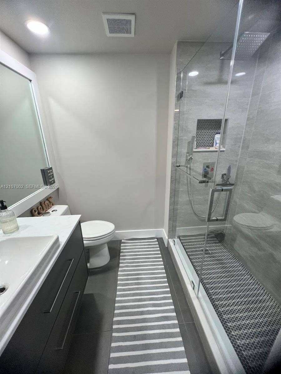 Modern vanity with a rectangular basin, quartz countertop, glass-enclosed shower with a rainfall showerhead, and a tiled shower niche