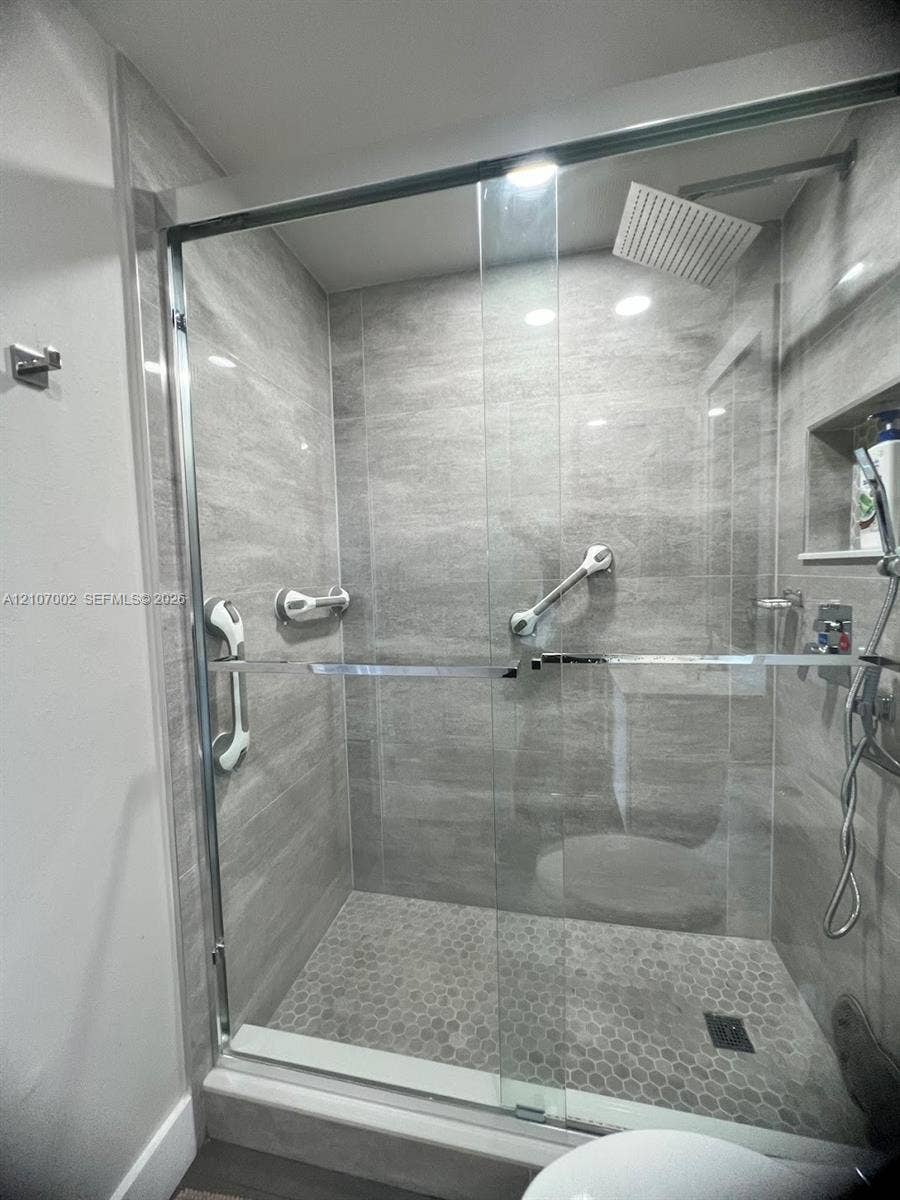Walk-in shower with floor-to-ceiling large-format tile, frameless glass enclosure, rainfall shower head, integrated wall niche, and hexagonal tile flooring