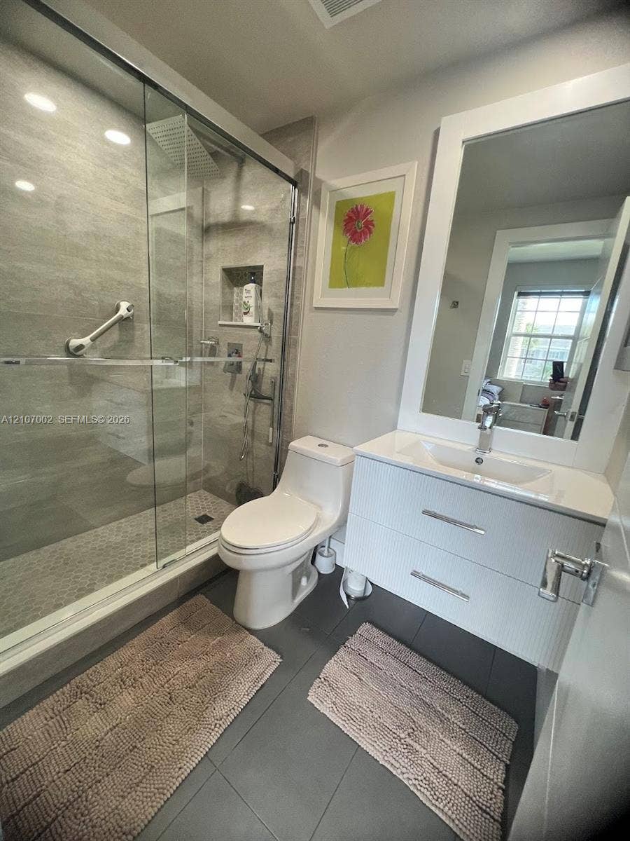 Walk-in shower with floor-to-ceiling tile, built-in recessed shelf, and glass enclosure, featuring a wall-mounted floating vanity, white countertop, and large rectangular mirror