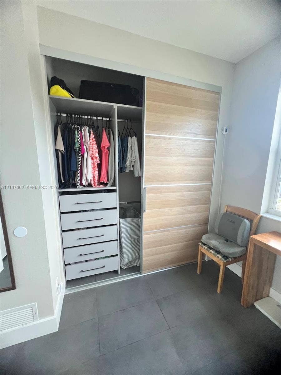 Closet featuring wood-finish sliding doors, built-in shelving, and integrated five-drawer dresser with matte hardware