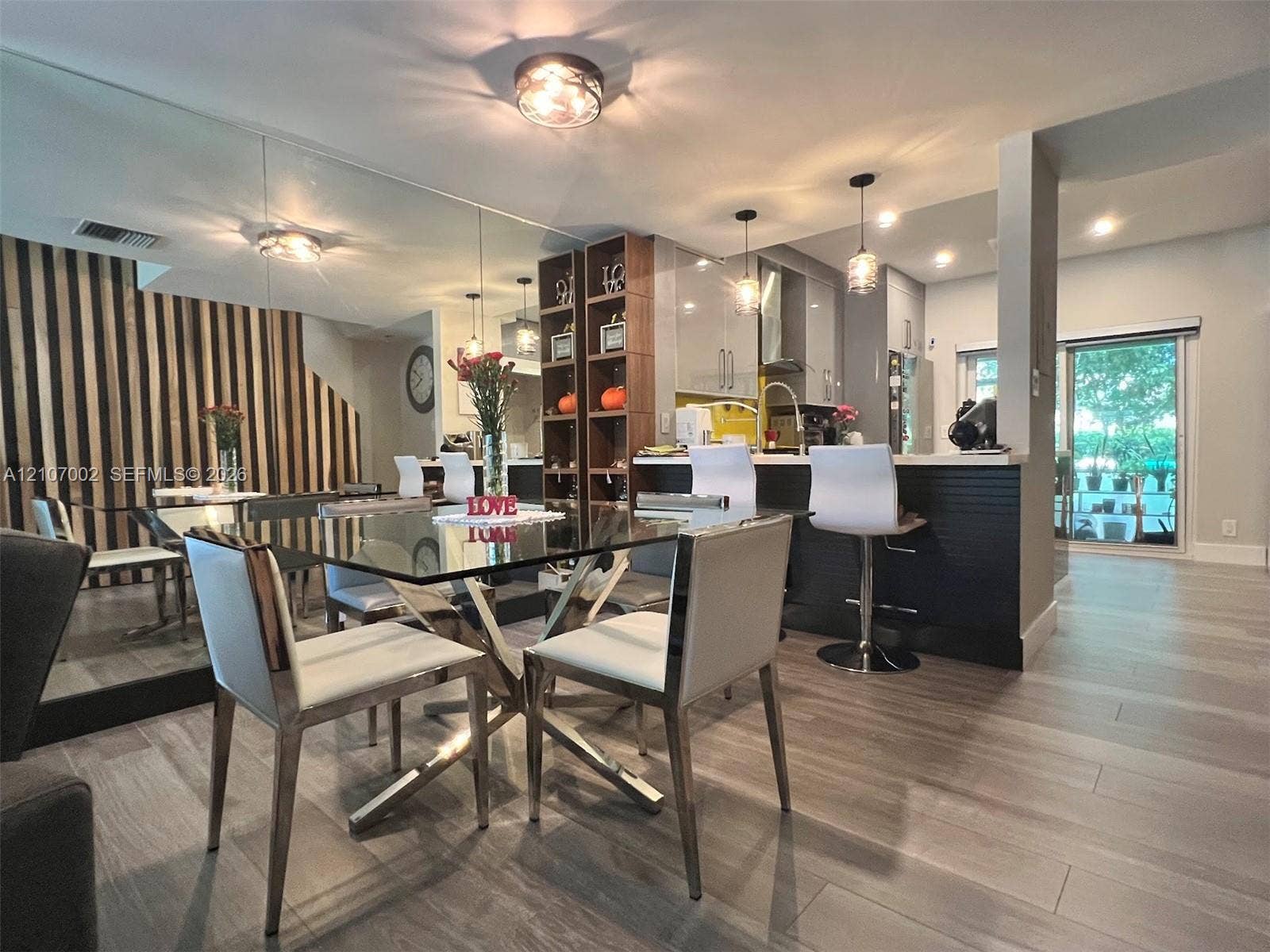 Interior space featuring wood-finish flooring, a floor-to-ceiling mirrored wall, vertical slat wood wall paneling, a kitchen island with stone countertop, and two glass pendant lights