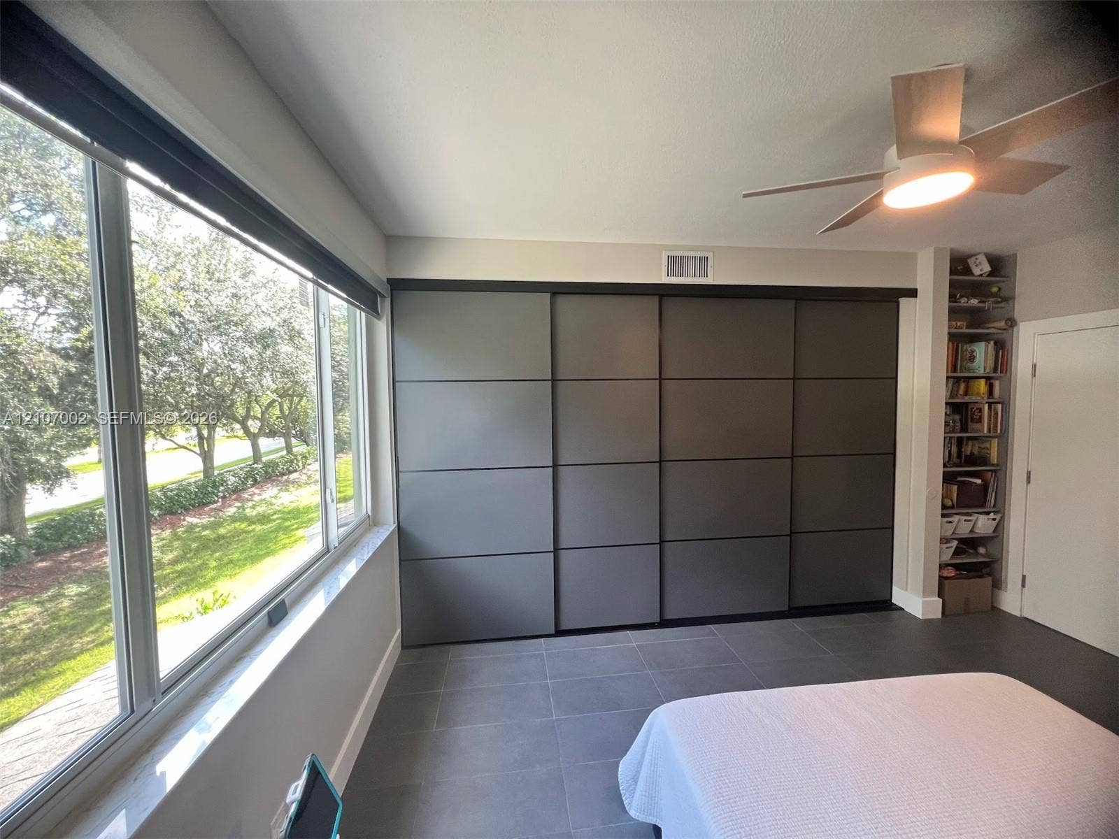 Expansive windows with exterior scenery, sliding panel closet doors, tile flooring, built-in recessed shelving, and a ceiling fan with integrated lighting
