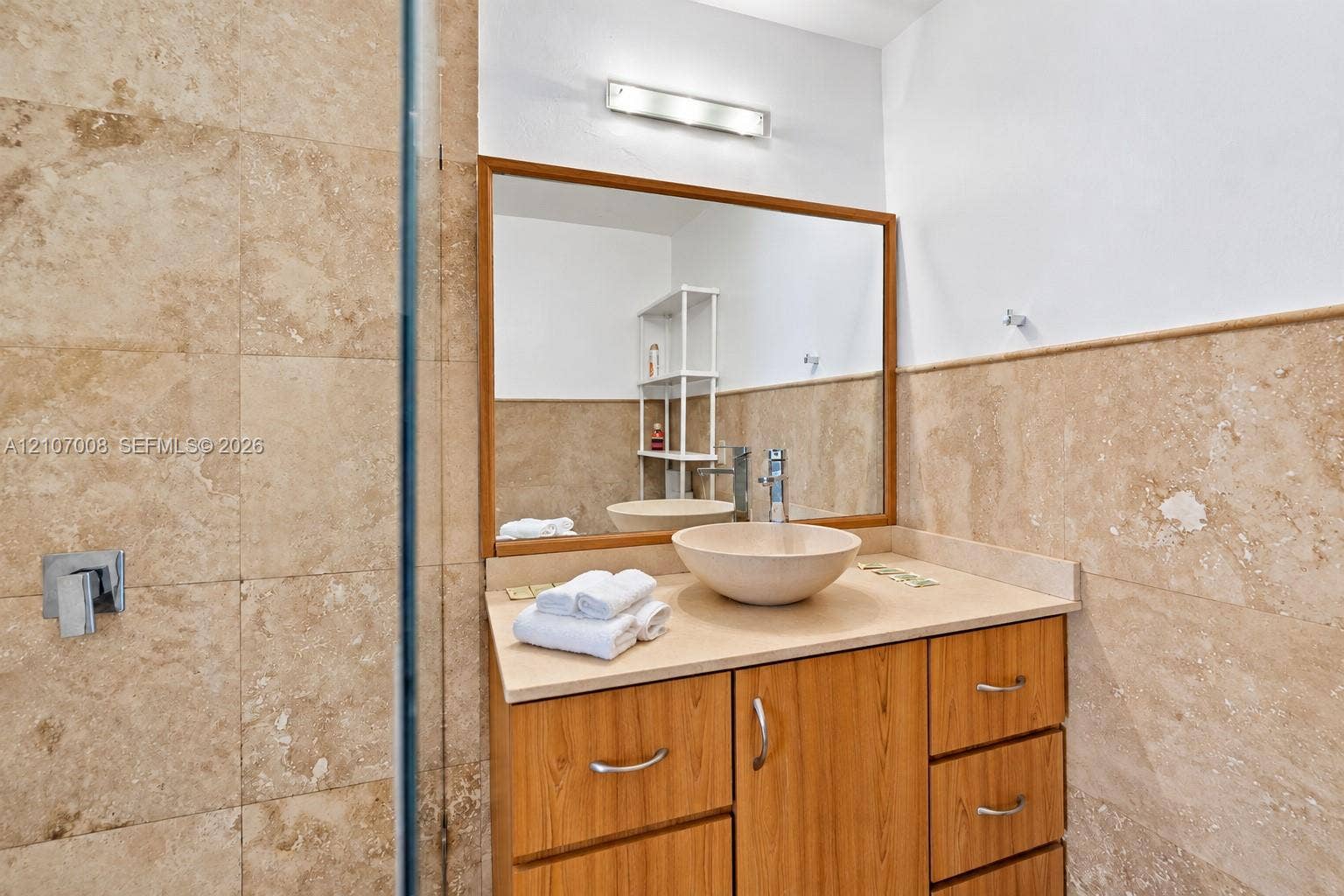 3030 Collins Avenue, #2H, Miami Beach, FL 33140 Vanity featuring wood-finish cabinetry, a stone-composite countertop, a circular vessel sink, a chrome single-handle faucet, and large-format neutral-toned tile wall cladding