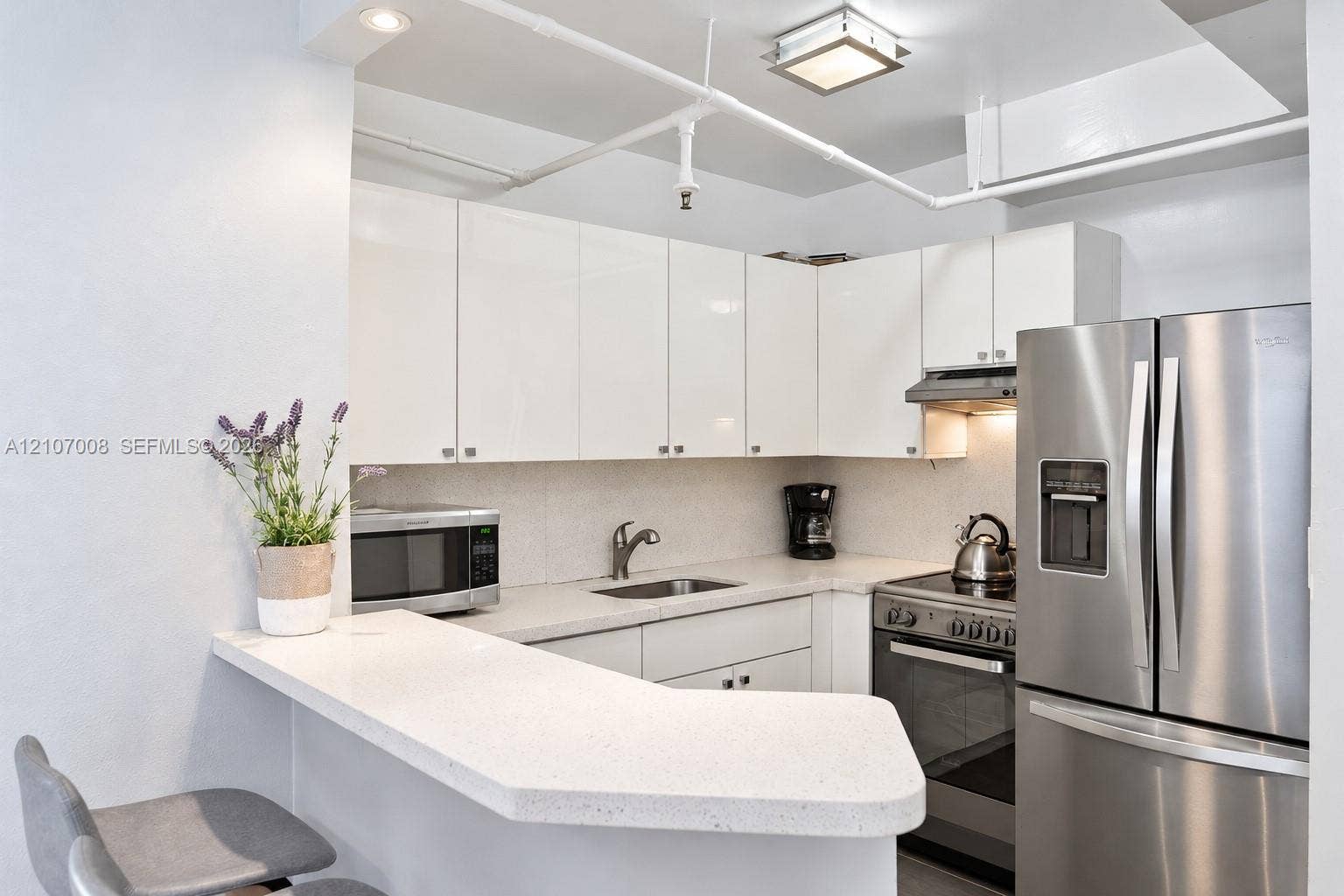 3030 Collins Avenue, #2H, Miami Beach, FL 33140 Kitchen featuring high-gloss white cabinetry, white stone countertops, stainless steel appliances, and integrated ceiling lighting