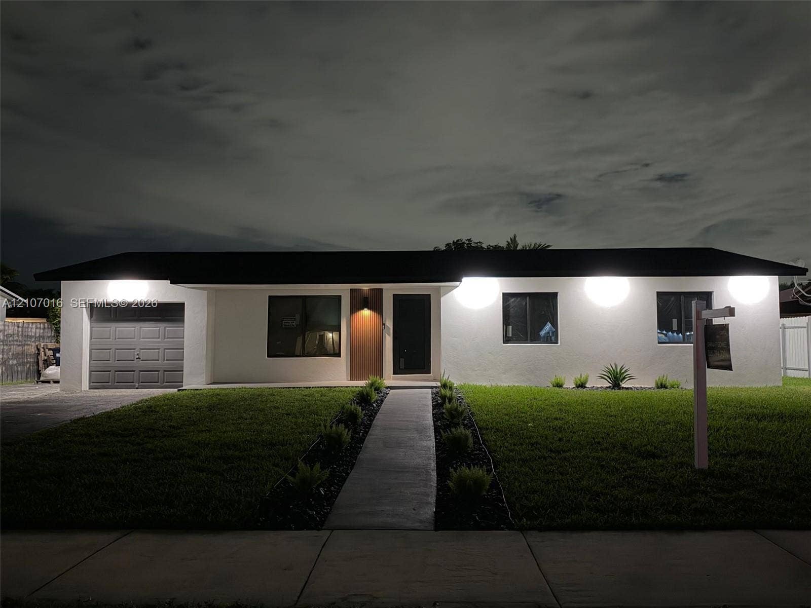Single-story exterior featuring a smooth stucco finish, a one-car garage, and a straight concrete walkway lined with landscaping beds