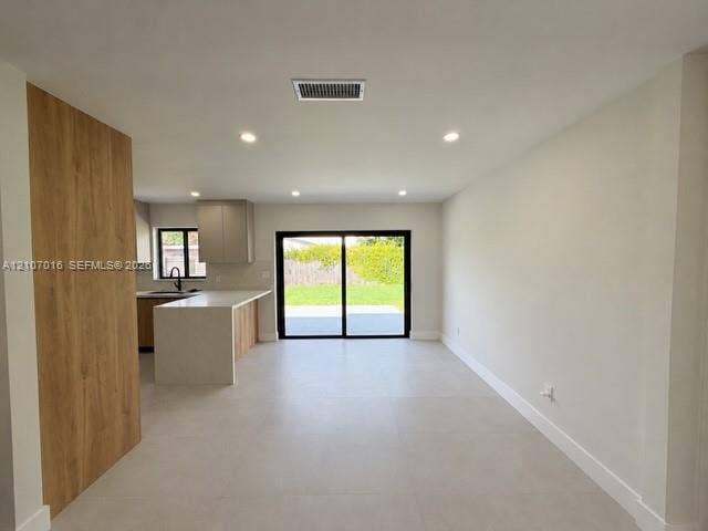 Open floor plan featuring large-format tile flooring, recessed lighting, wood-finish paneling, and a kitchen peninsula with stone-finish countertops and sliding glass doors
