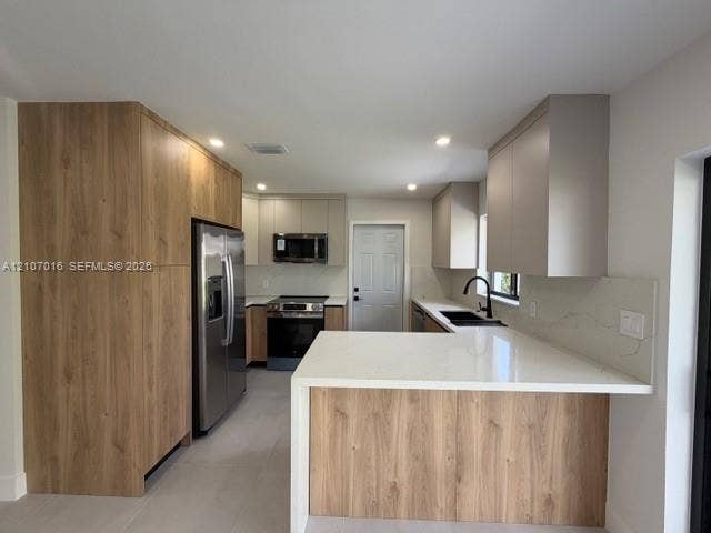 Kitchen featuring two-tone cabinetry with wood-finish accents, quartz countertops, integrated stainless steel appliances, and a matte black faucet