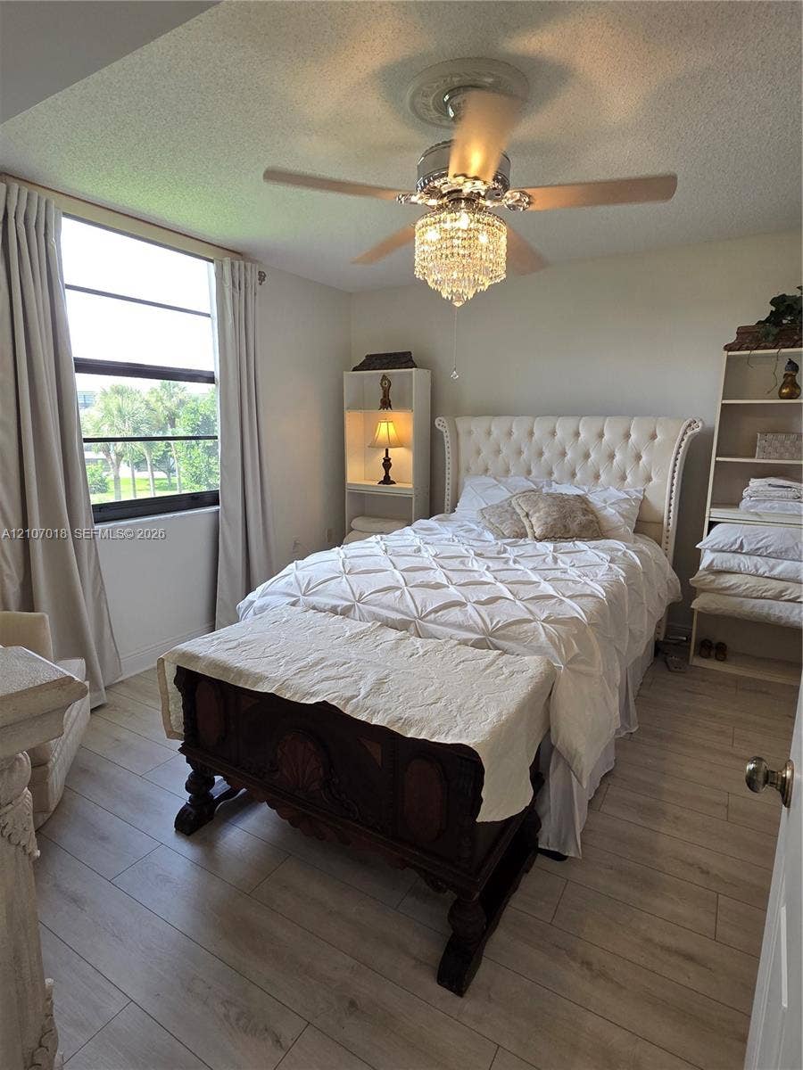 3716 Whitehall Drive, #304, West Palm Beach, West Palm Beach, FL 33401 Wood-finish flooring, large-format window with dark trim, and a ceiling-mounted crystal chandelier fan