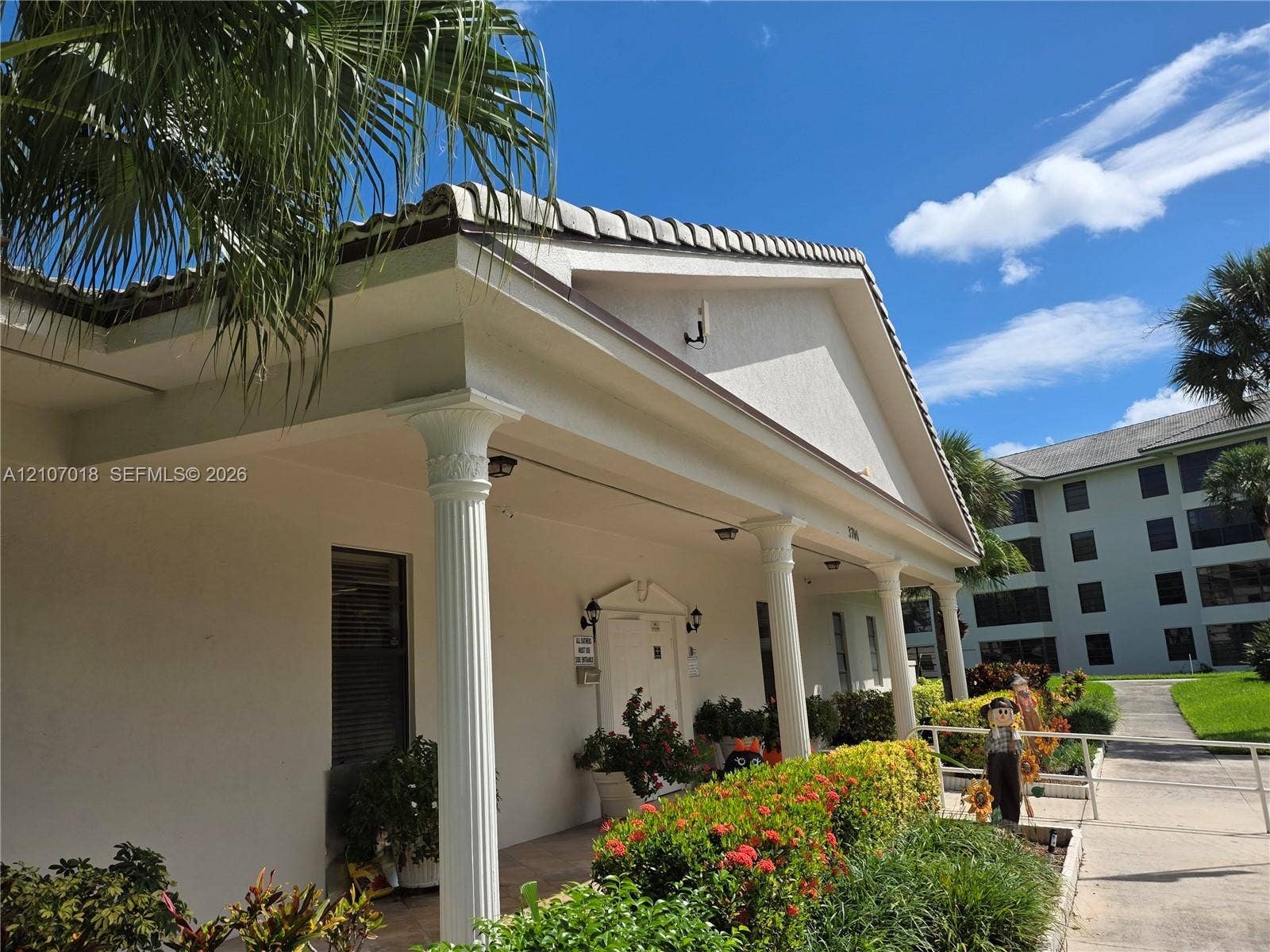 3716 Whitehall Drive, #304, West Palm Beach, West Palm Beach, FL 33401 Exterior facade featuring a covered entryway with classic columns, a pitched tile roof, and a textured stucco finish