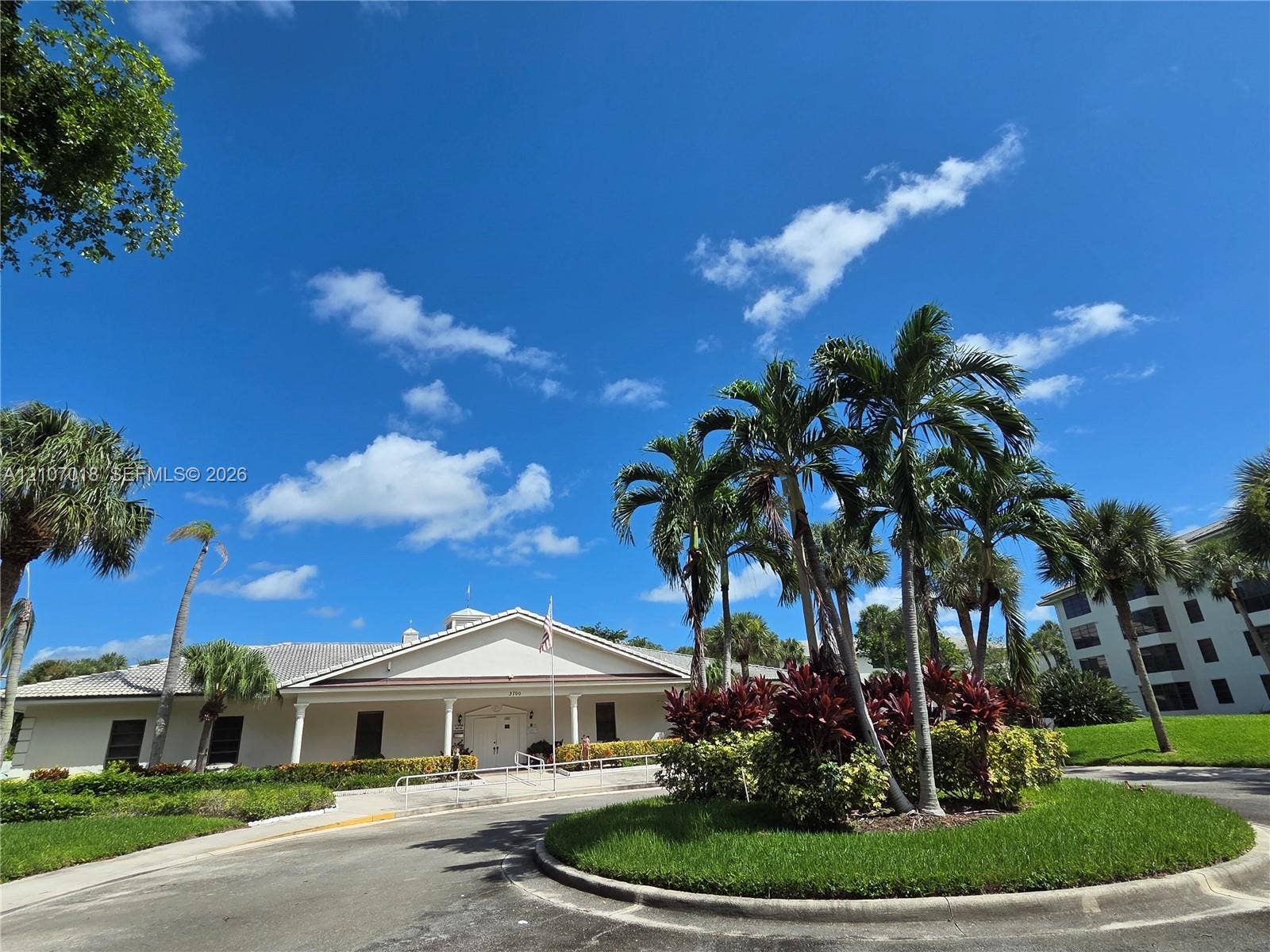 3716 Whitehall Drive, #304, West Palm Beach, West Palm Beach, FL 33401 Exterior featuring a light-toned stucco faade, a multi-gabled roofline, covered entryway with support columns, and mature tropical landscaping