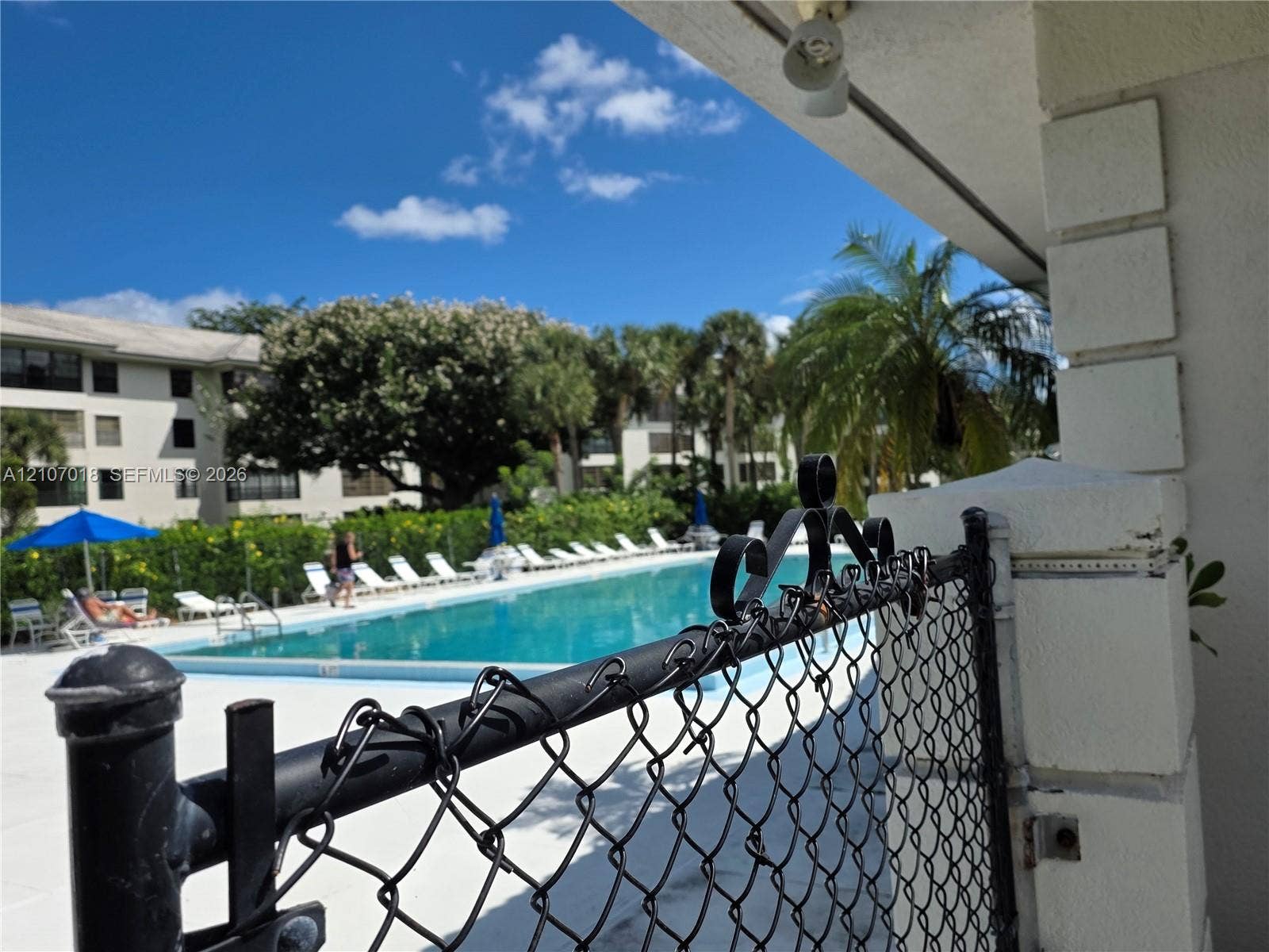 3716 Whitehall Drive, #304, West Palm Beach, West Palm Beach, FL 33401 Swimming pool with concrete decking, secured by a metal chain-link perimeter fence and surrounded by mature palm trees and established landscaping