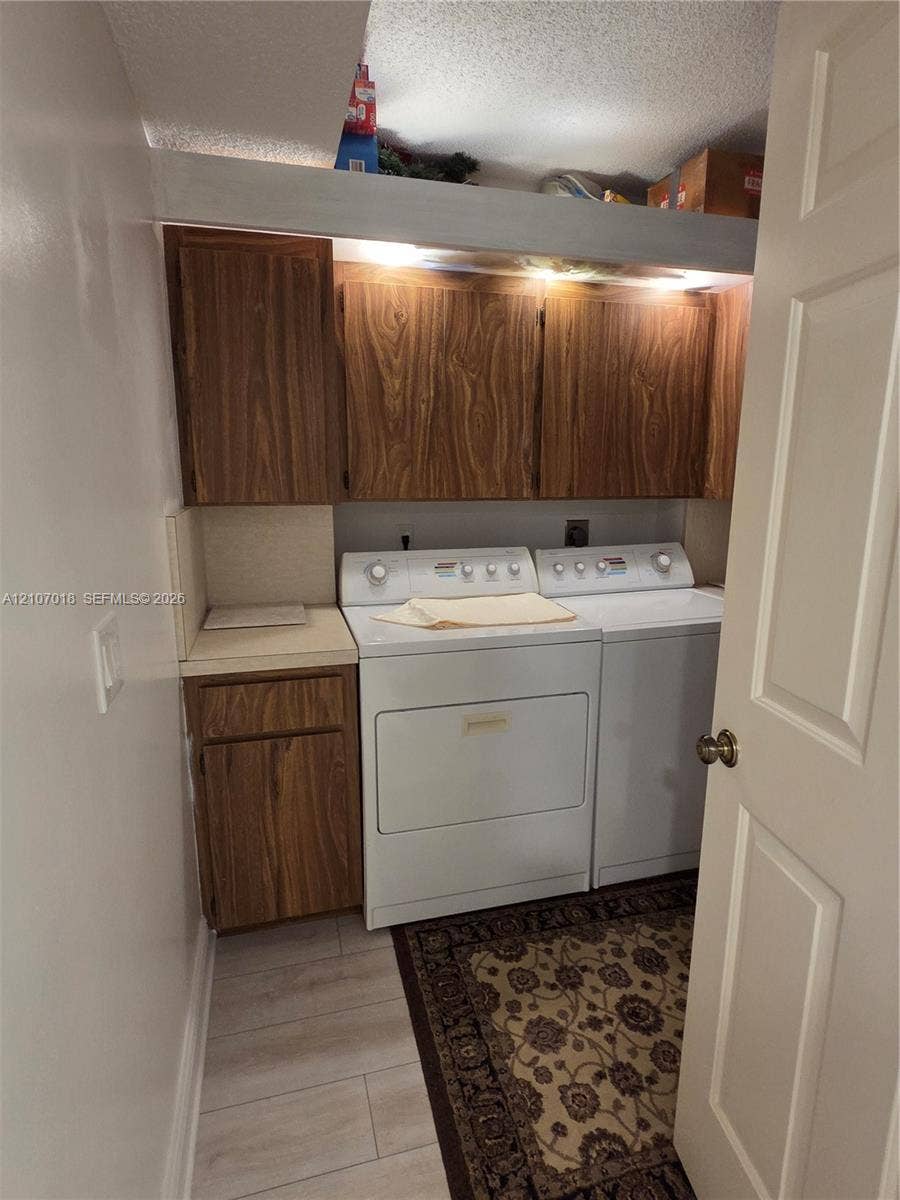3716 Whitehall Drive, #304, West Palm Beach, West Palm Beach, FL 33401 Laundry area featuring wood-finish cabinetry, neutral solid-surface countertop, and light-tone plank flooring