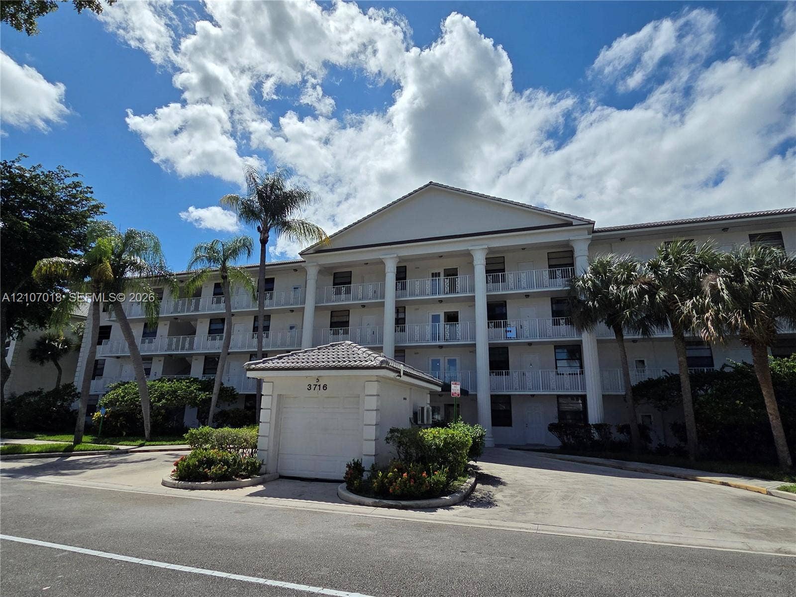 3716 Whitehall Drive, #304, West Palm Beach, West Palm Beach, FL 33401 Multi-story building exterior featuring a classic pediment, full-height white columns, multi-level railed balconies, and a detached garage structure