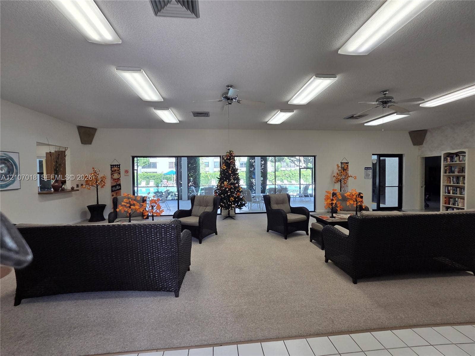 3716 Whitehall Drive, #304, West Palm Beach, West Palm Beach, FL 33401 Common area featuring wall-to-wall carpeting, multiple ceiling-mounted fluorescent light fixtures, ceiling fans, built-in shelving, and floor-to-ceiling windows