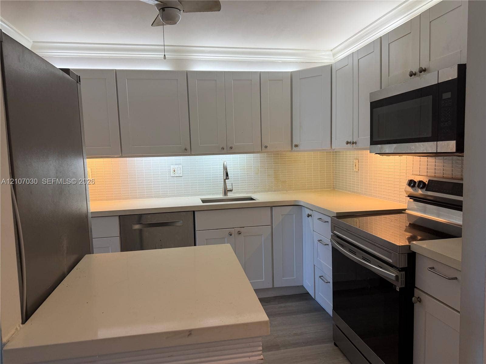 Kitchen featuring white shaker-style cabinetry, solid-surface countertops, a tiled backsplash, wood-finish flooring, and stainless steel appliances