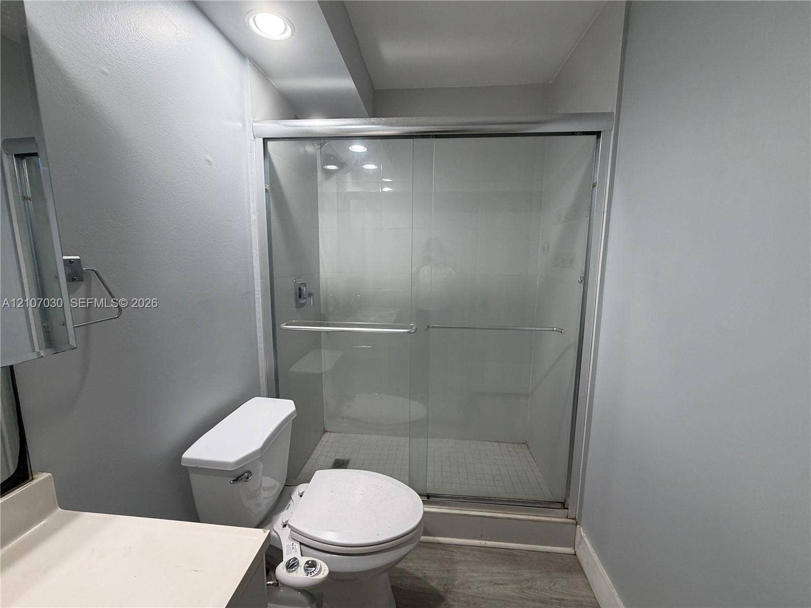Shower enclosure with sliding glass doors, tiled floor, recessed lighting, and white toilet