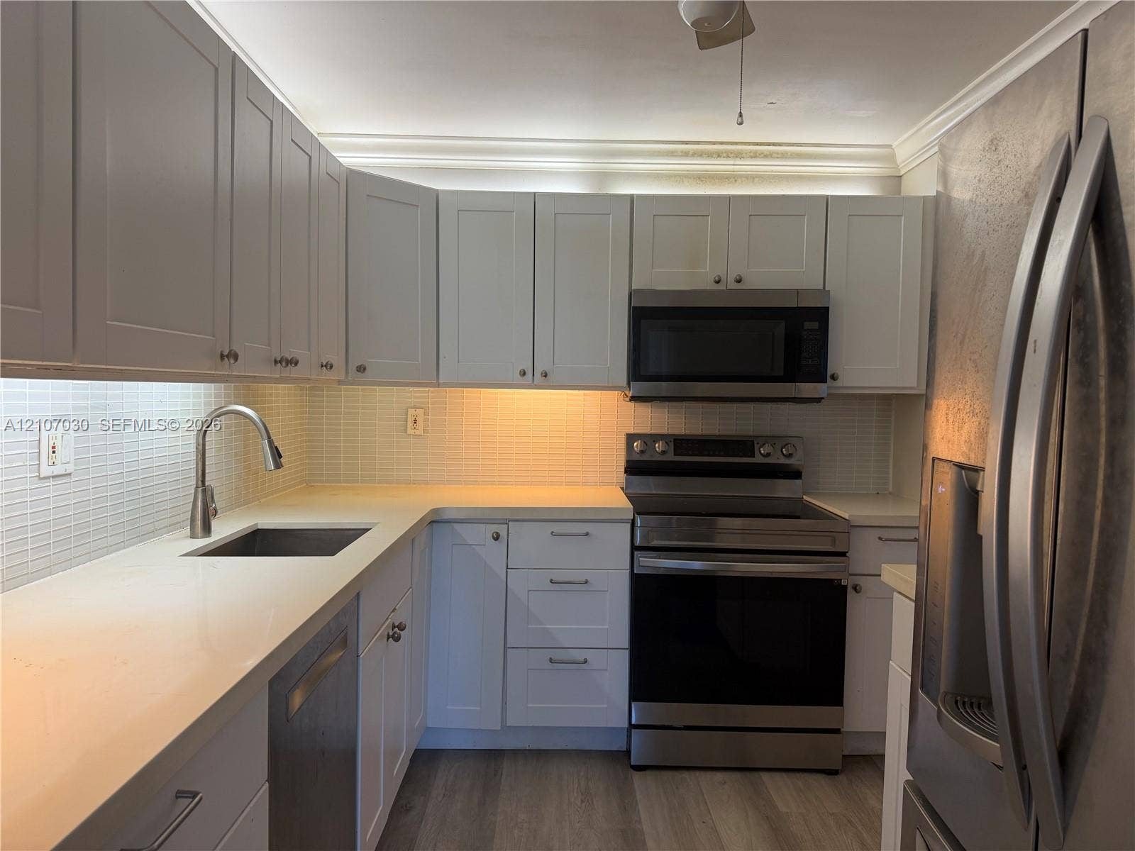 Shaker-style cabinetry, quartz countertops, tile backsplash, stainless steel appliances, and wood-finish flooring