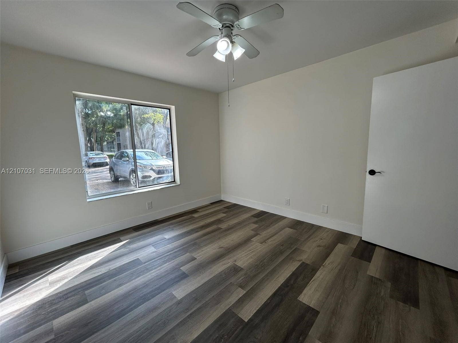 Room featuring wood-finish flooring, a neutral color palette, a sliding window, and a ceiling-mounted light fixture with a fan