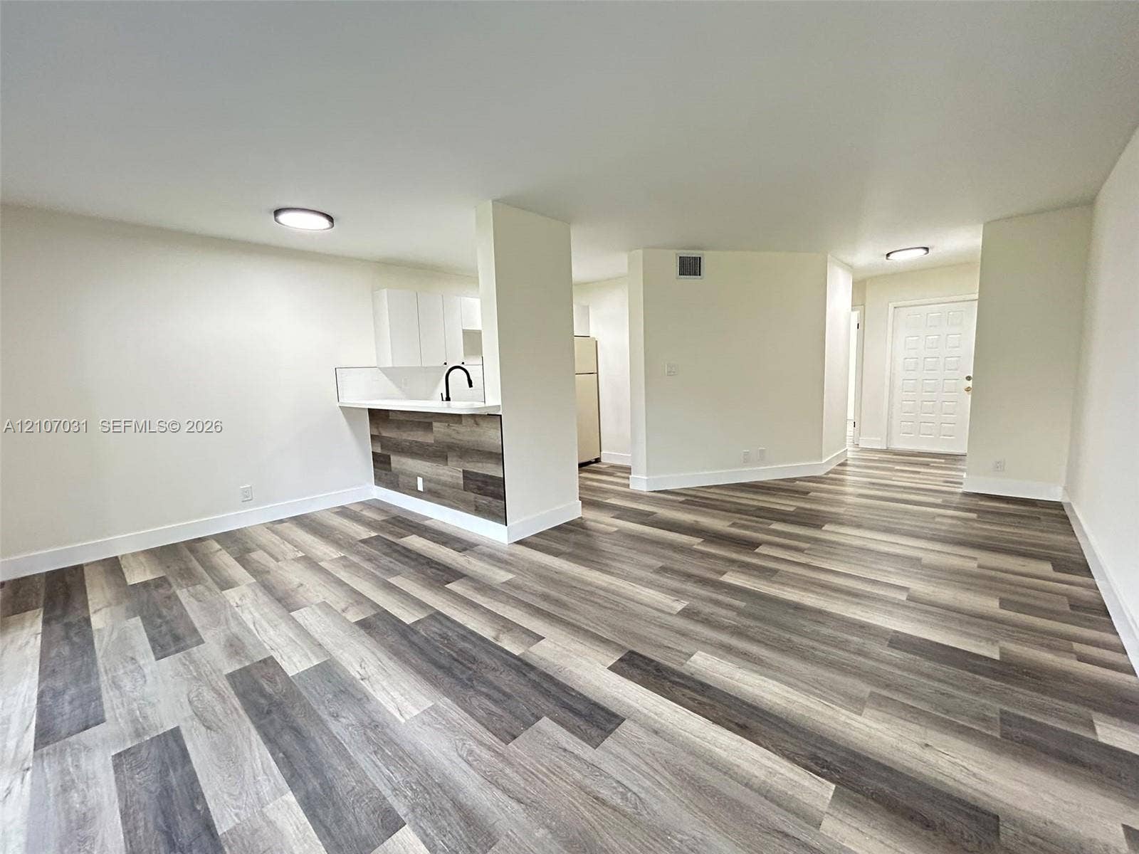 Wood-finish flooring, kitchen peninsula with wood-finish paneling, white cabinetry, matte black faucet, and flush-mount ceiling lighting