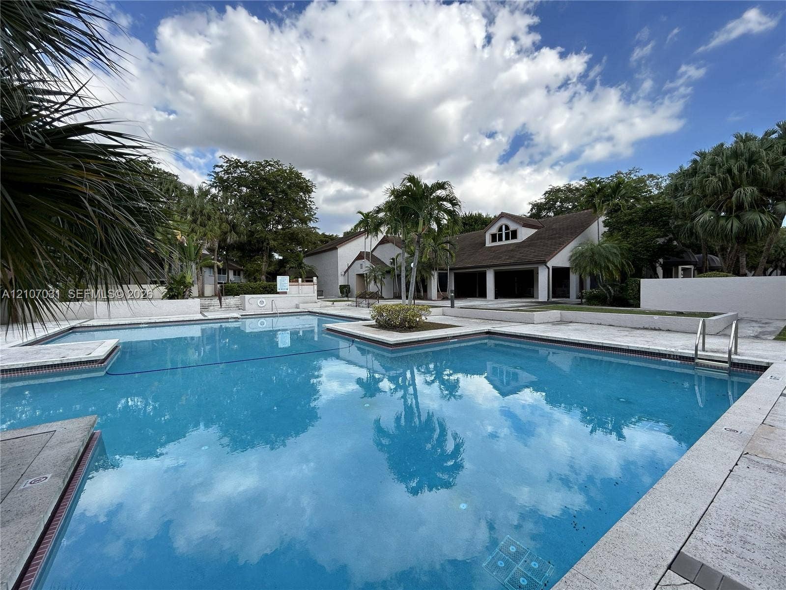 In-ground swimming pool with stone-tiled decking, integrated landscape island, metal pool ladder, and manicured palm trees