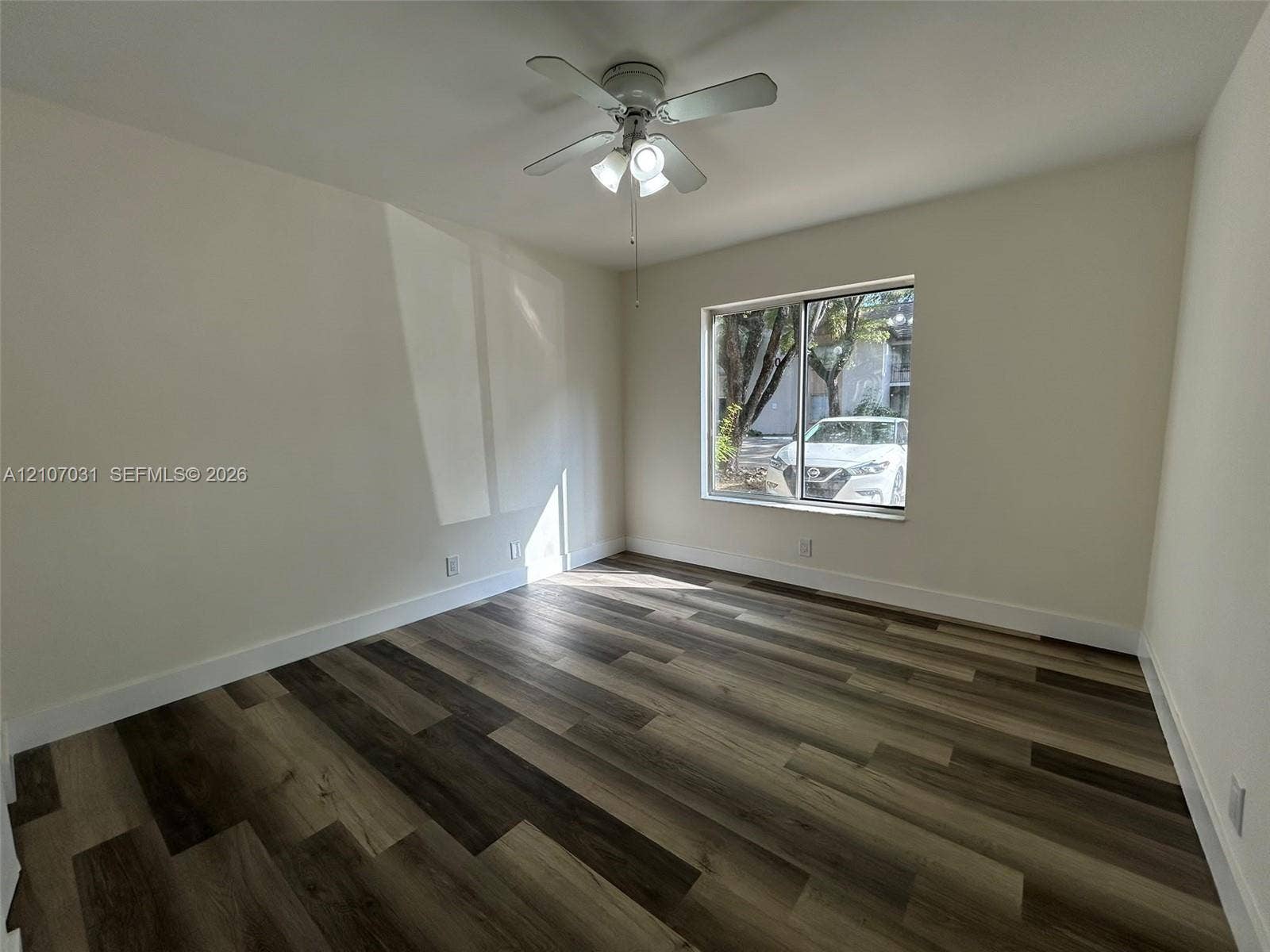 Interior room featuring wood-finish flooring, neutral walls, and a ceiling-mounted light fixture with a multi-blade fan