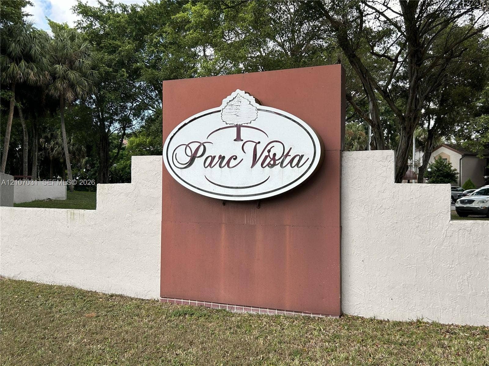 Parc Vista monument sign featuring a terracotta-finish center panel, white stucco stepped-wall masonry, and mature tree landscaping