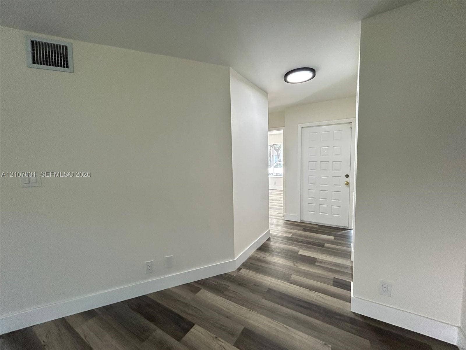 Interior entryway featuring multi-tonal wood-finish flooring, a white paneled door, and flush-mount ceiling lighting