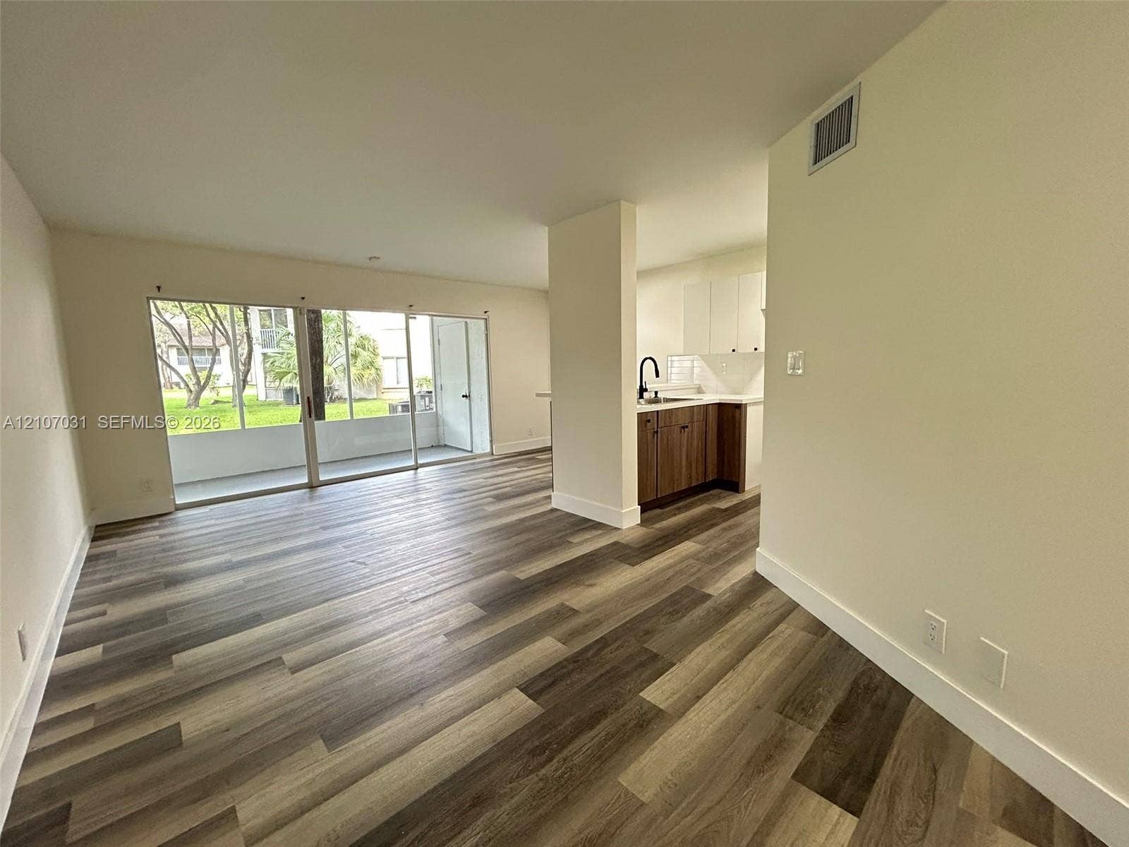 Wood-finish flooring, floor-to-ceiling sliding glass doors, kitchen featuring white upper cabinetry, lower wood-tone cabinetry, and matte black plumbing fixtures
