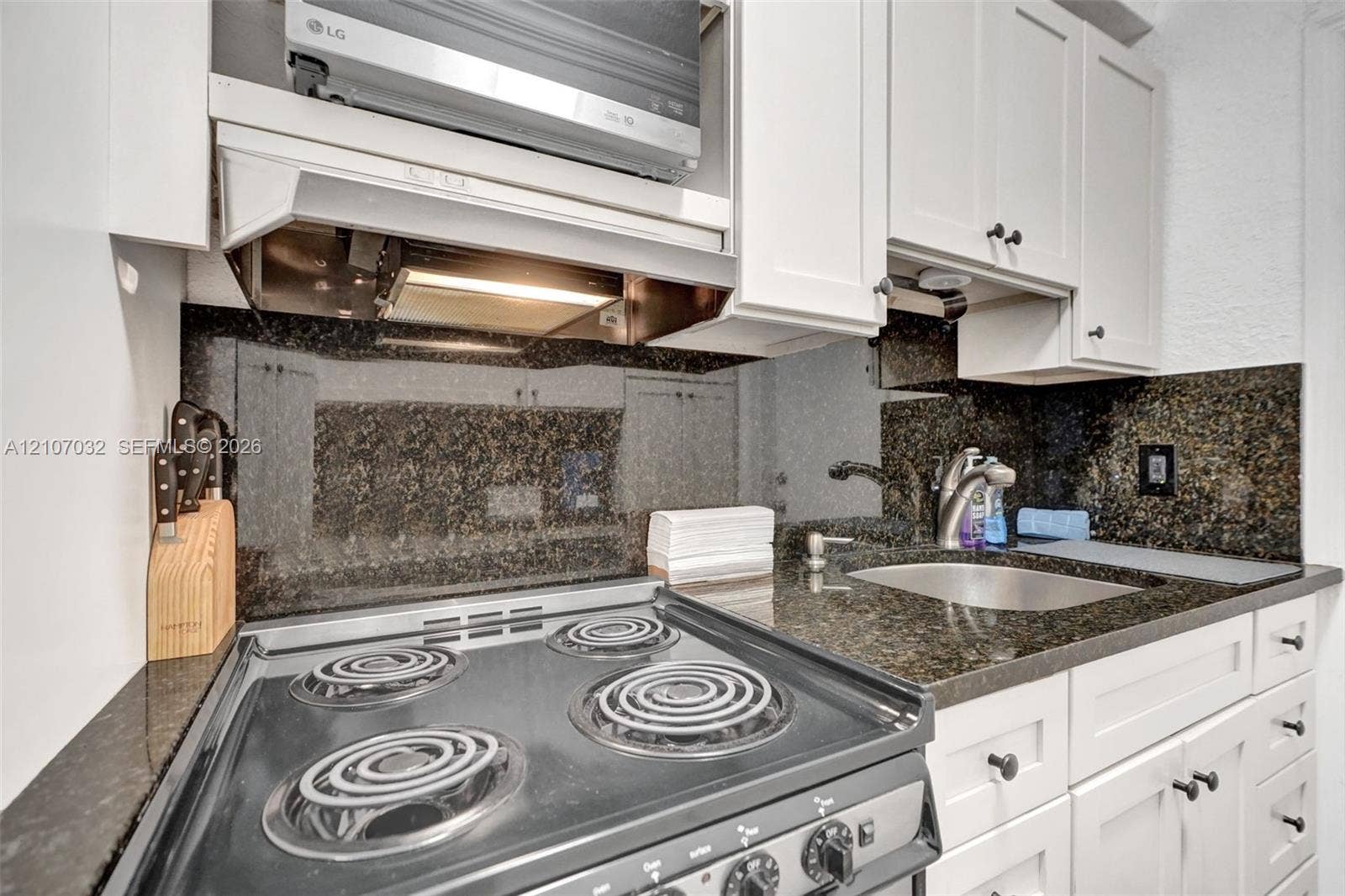 443 NE 17th Way, Fort Lauderdale, FL 33301 Kitchen featuring white cabinetry, dark stone countertops, integrated backsplash, stainless steel electric range, and an under-mounted sink
