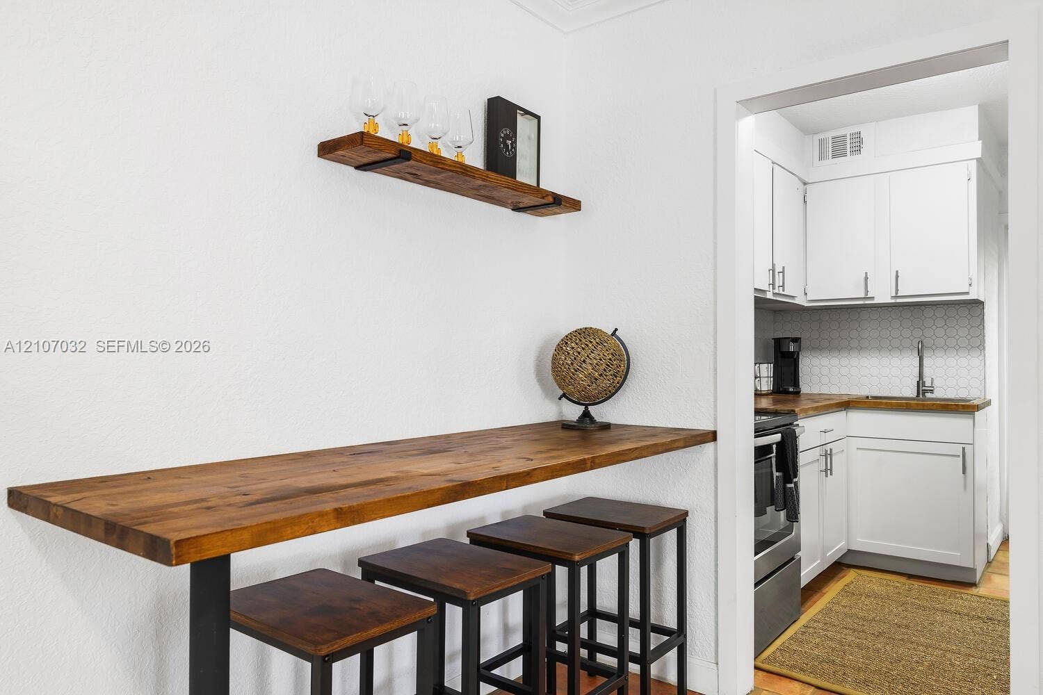 443 NE 17th Way, Fort Lauderdale, FL 33301 Wall-mounted wooden shelving, custom wood-surfaced breakfast bar, and white shaker-style cabinetry with geometric tile backsplash