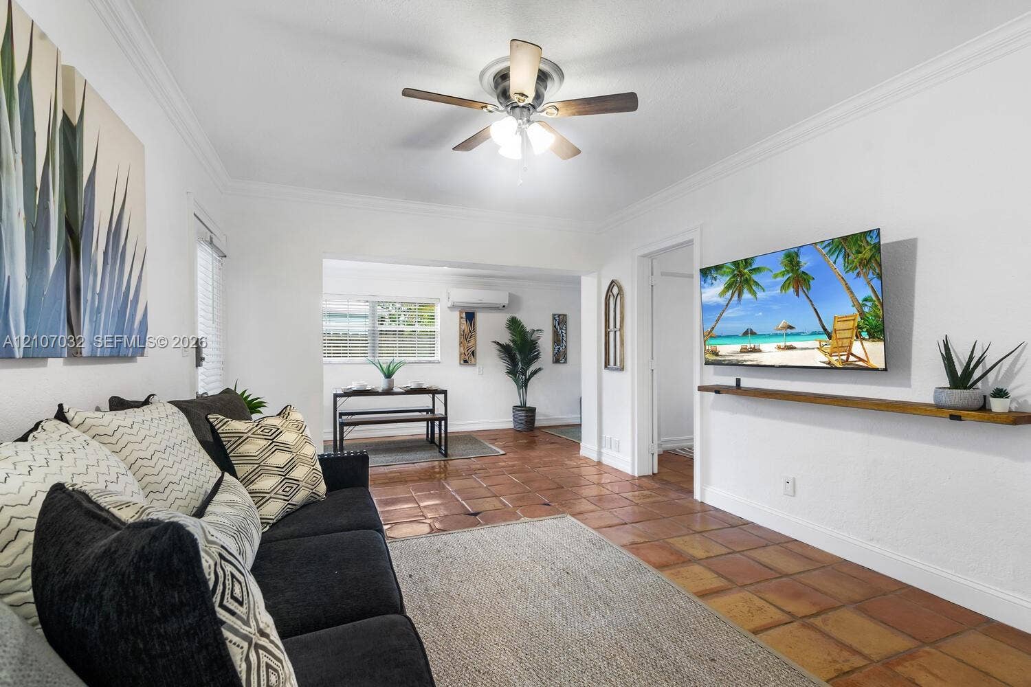 443 NE 17th Way, Fort Lauderdale, FL 33301 Living space featuring terracotta tile flooring, crown molding, a central ceiling fan with integrated lighting, and a wall-mounted wooden display shelf