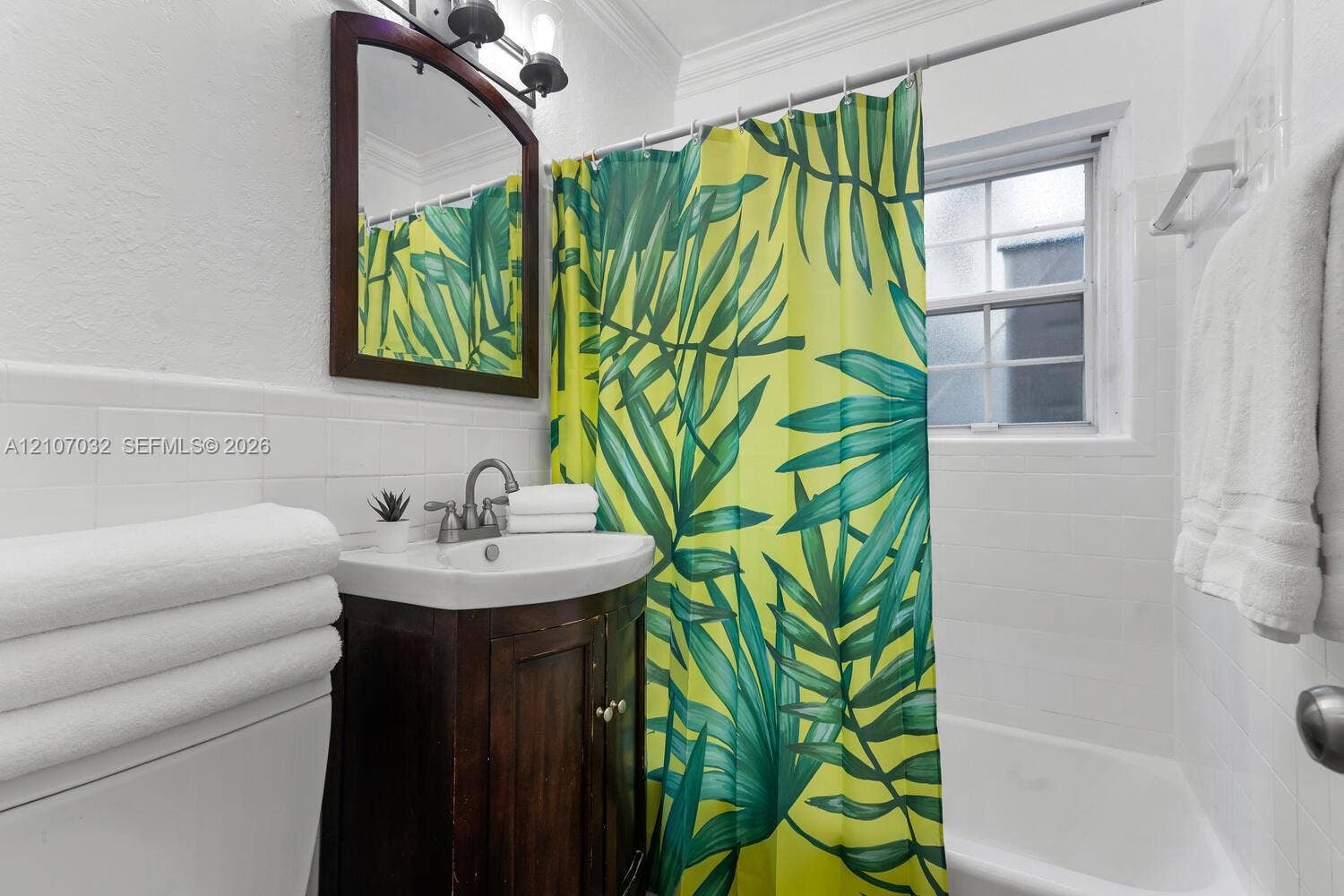 443 NE 17th Way, Fort Lauderdale, FL 33301 Bathroom featuring a dark wood-finish vanity, white ceramic sink with chrome hardware, arched wall-mounted mirror, and white tile wainscoting