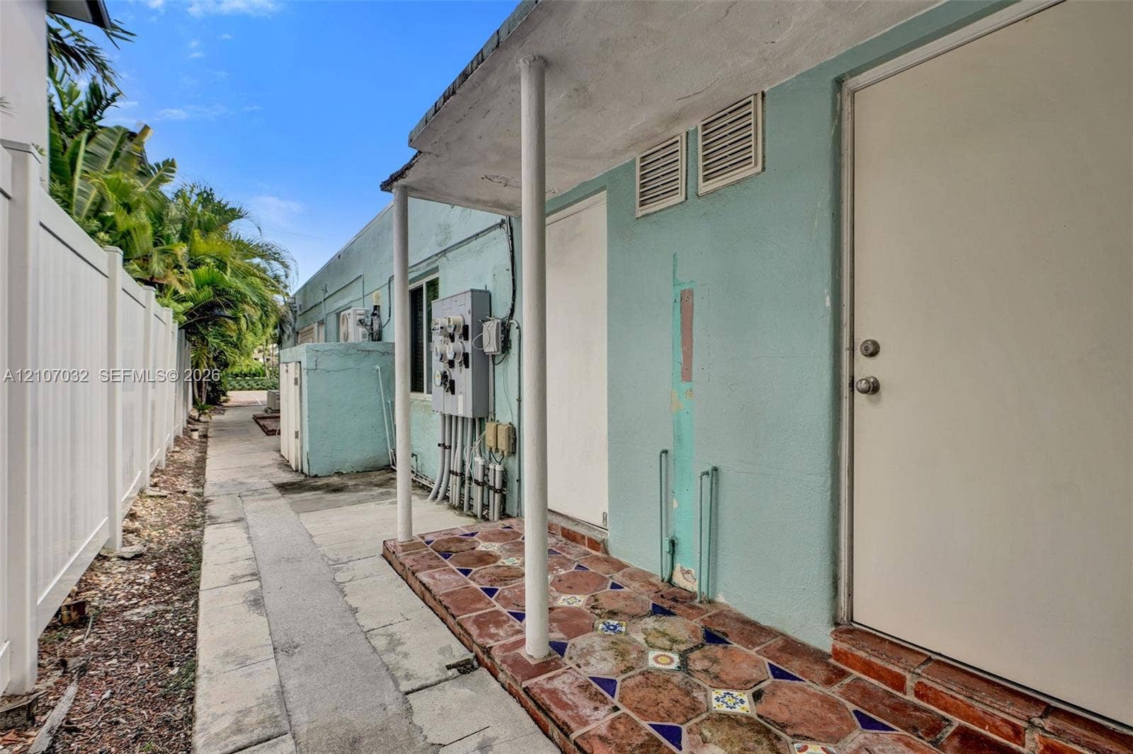 443 NE 17th Way, Fort Lauderdale, FL 33301 Exterior side entry featuring a covered porch with decorative patterned tile flooring, supported by round structural columns and enclosed by a tall privacy fence