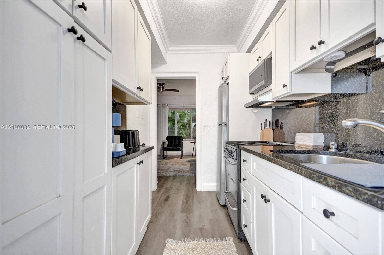 443 NE 17th Way, Fort Lauderdale, FL 33301 Galley kitchen featuring white shaker-style cabinetry, stone countertops, integrated stainless steel appliances, dark stone backsplash, and wood-finish flooring