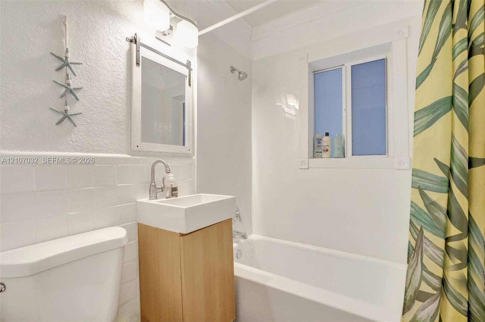 443 NE 17th Way, Fort Lauderdale, FL 33301 Bathroom featuring a wall-mounted vanity with a rectangular basin, subway tile wainscoting, sliding barn-door style mirror, and a built-in bathtub with shower surround