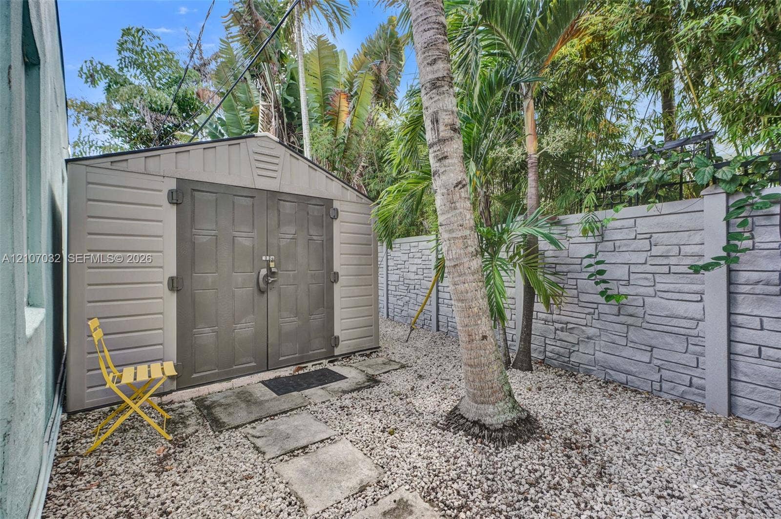 443 NE 17th Way, Fort Lauderdale, FL 33301 Exterior storage shed featuring dual-panel doors, accompanied by a stone-pattern privacy wall, stone paver pathway, and gravel ground cover