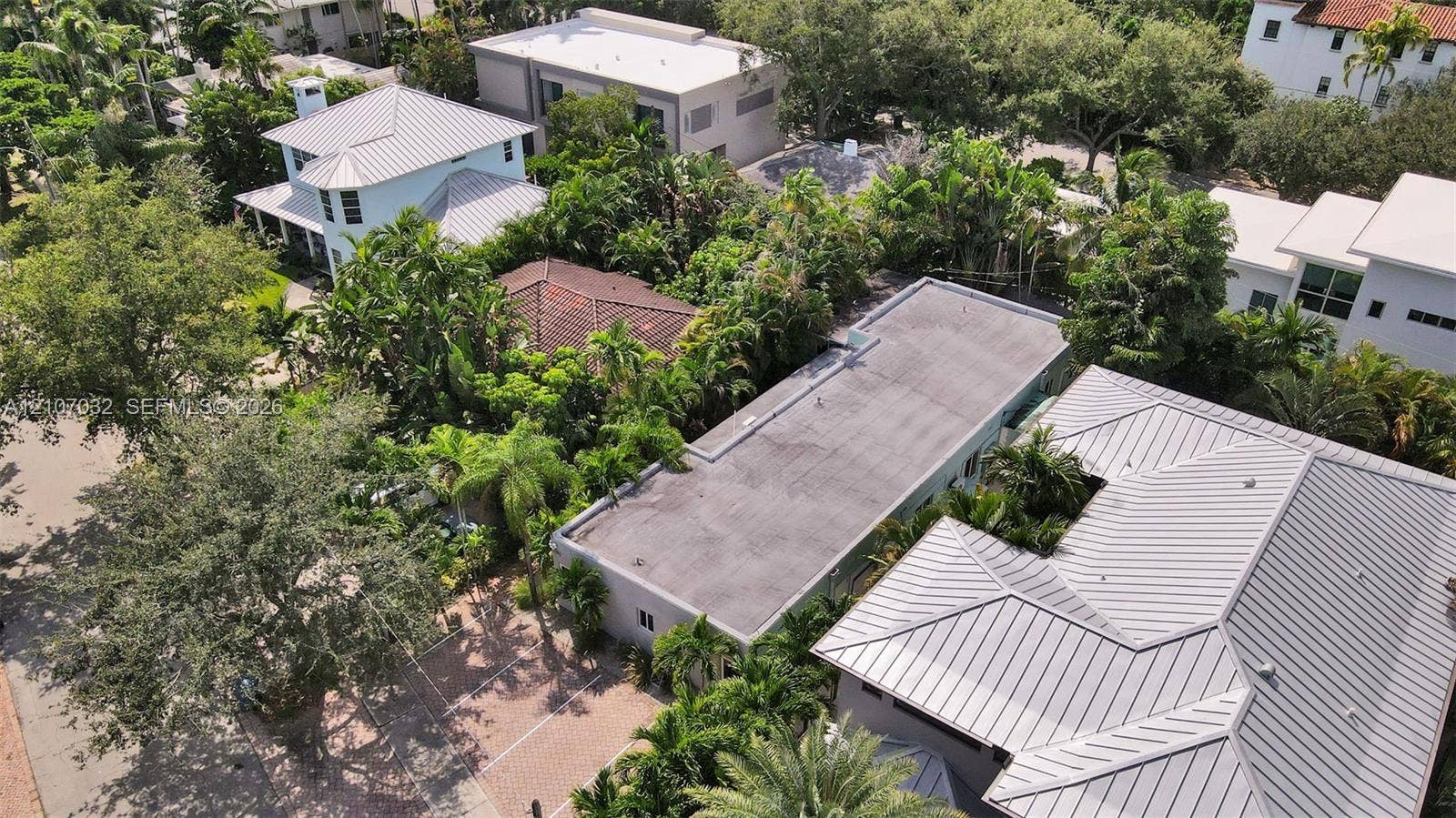443 NE 17th Way, Fort Lauderdale, FL 33301 Aerial perspective of a multi-structure property featuring metal roof systems, paver driveway, and mature landscaping