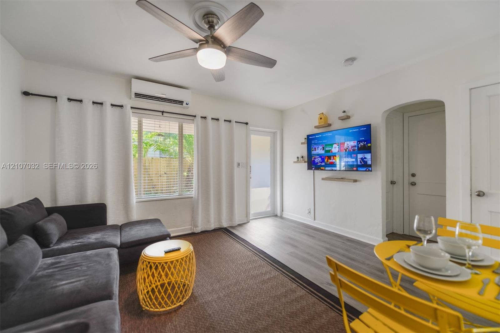 443 NE 17th Way, Fort Lauderdale, FL 33301 Room featuring wood-finish flooring, a wall-mounted ductless air conditioning unit, a multi-blade ceiling fan with integrated lighting, and an arched doorway