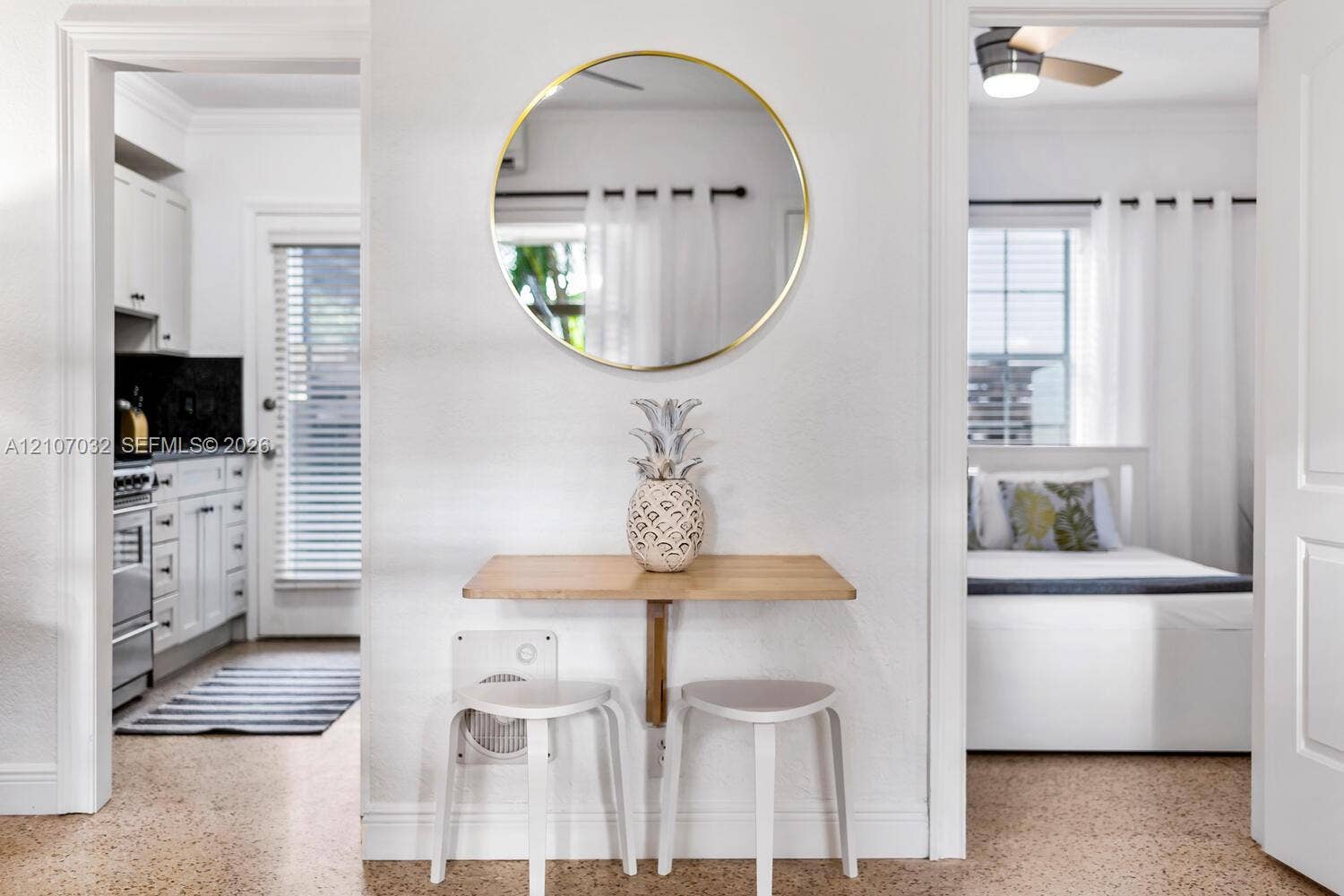 443 NE 17th Way, Fort Lauderdale, FL 33301 Wall-mounted wood-finish breakfast bar featuring a circular metallic-framed mirror, neutral flooring, and white cabinetry in the kitchen area