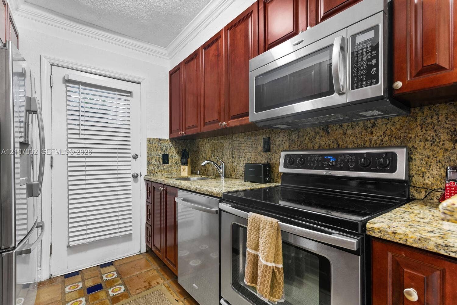 443 NE 17th Way, Fort Lauderdale, FL 33301 Kitchen featuring cherry-finish cabinetry, stone countertops, stainless steel appliances, and decorative tile flooring