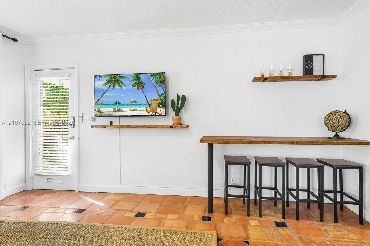 443 NE 17th Way, Fort Lauderdale, FL 33301 Terracotta tile flooring with inlaid decorative tiles, white interior walls, built-in wooden shelving, and a wall-mounted wooden counter with metal support legs